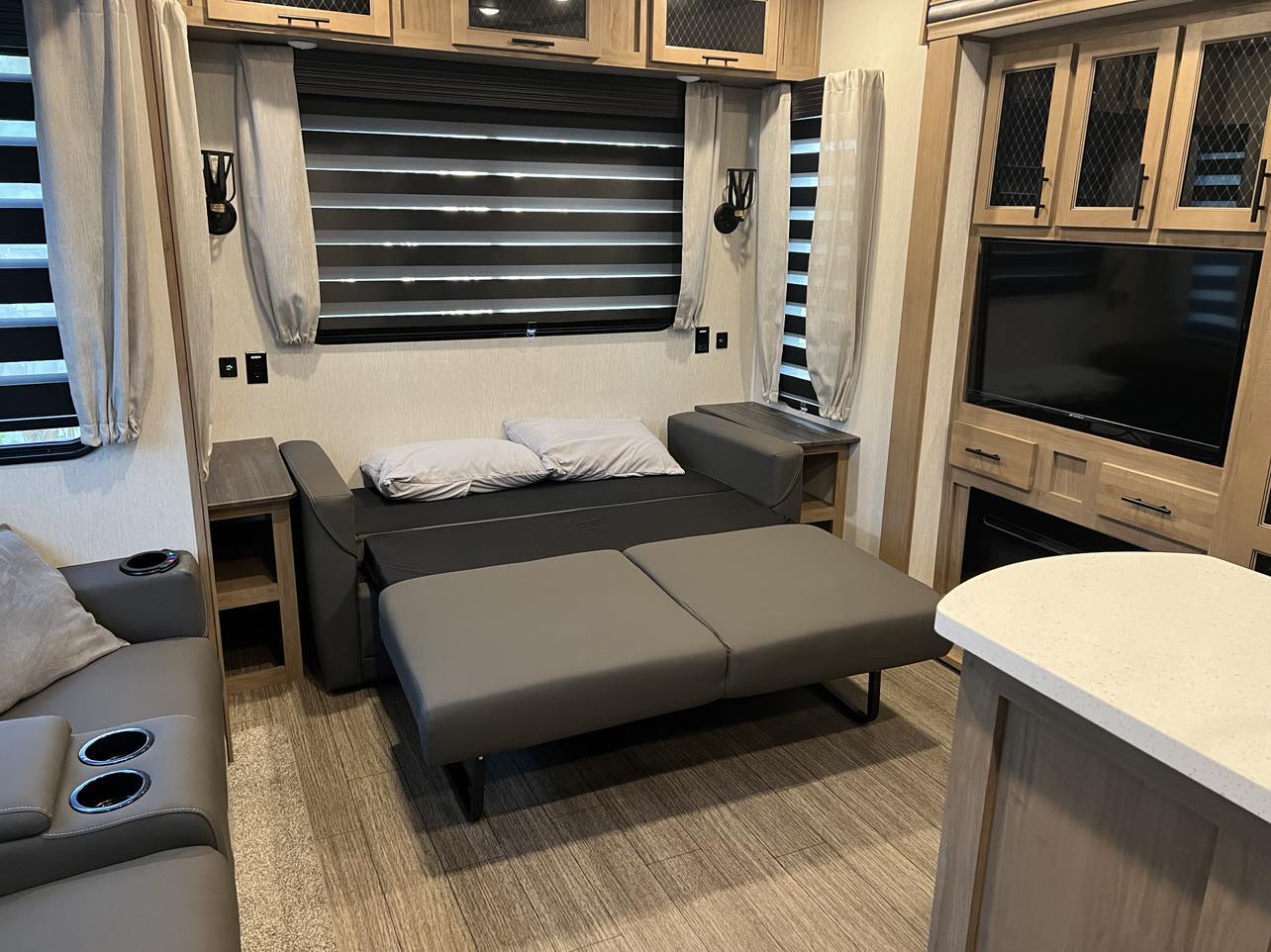 RV rental interior showcasing a pull-out sofa bed, built-in entertainment system with TV, and comfortable seating for guests.. Forest River Sabre 2023