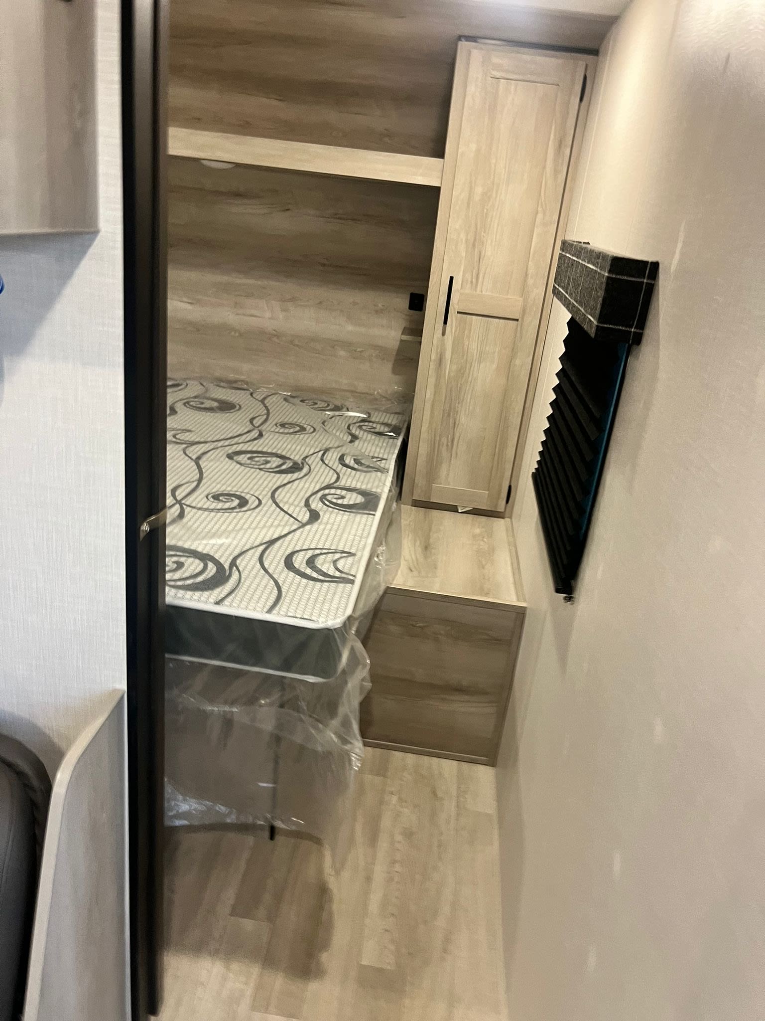 Inside an RV rental: a neat bedroom with a new mattress, overhead shelf, and built-in wardrobe for storage.. Other Other 2024