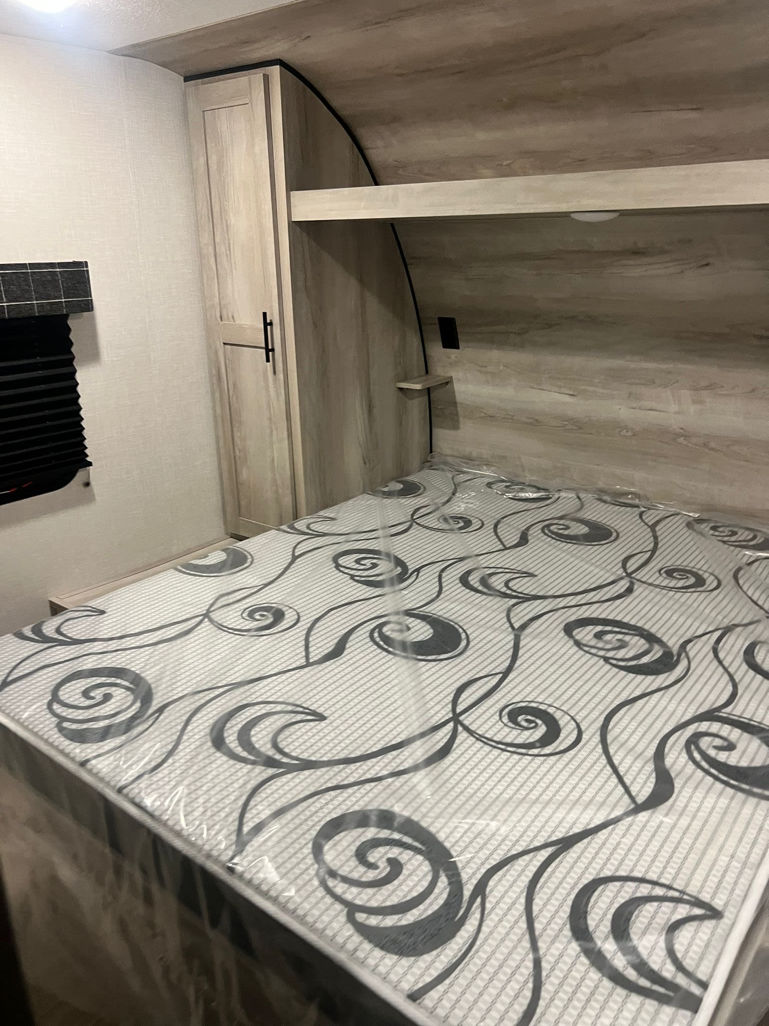 Inside a new RV rental bedroom, featuring a light-toned wood interior, wardrobe, window, and a mattress still wrapped in plastic.. Other Other 2024