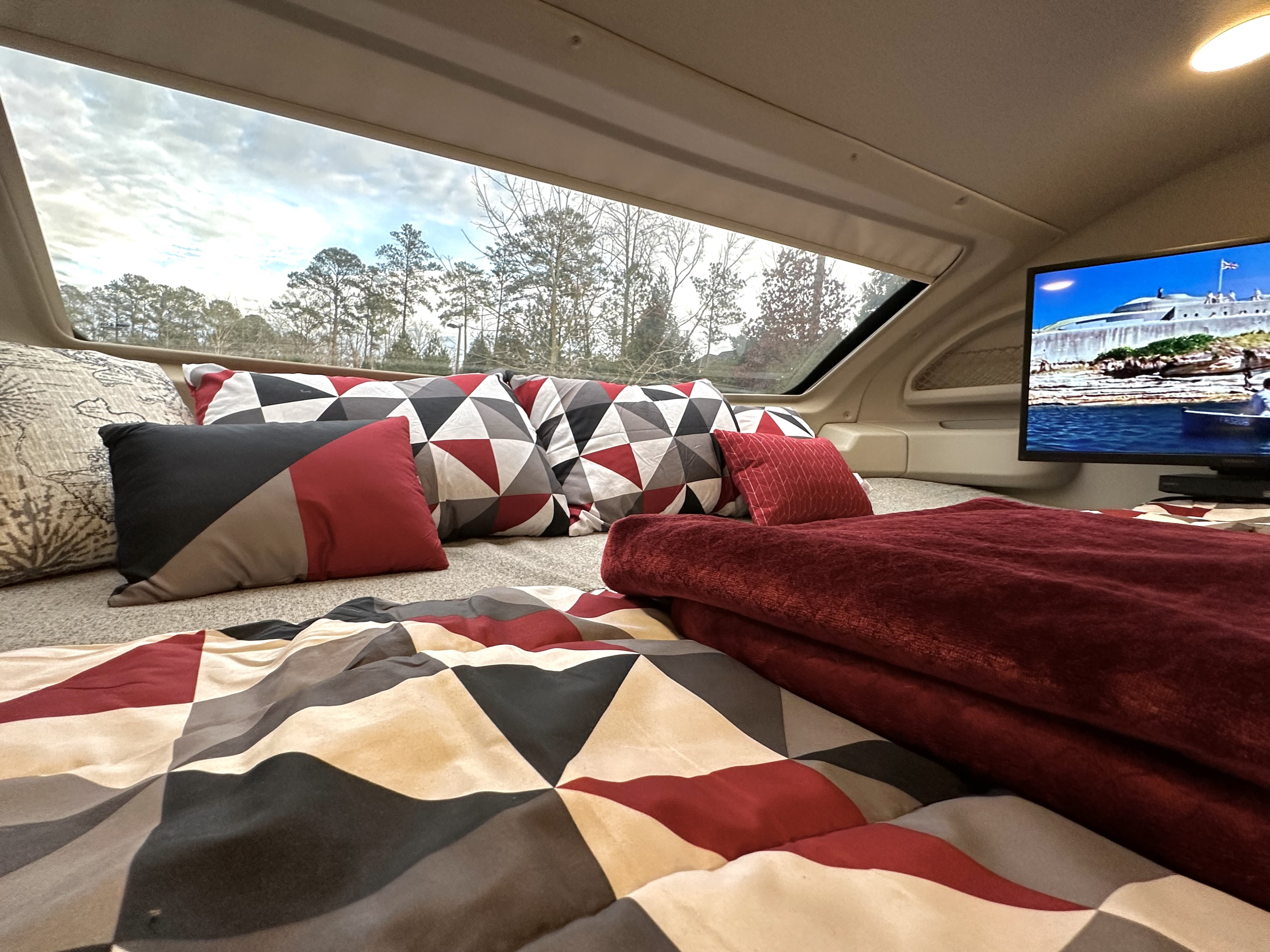 Cozy RV rental interior with geometric bedding, a TV, and a large window view of trees and sky.. Entegra Coach Esteem 2021