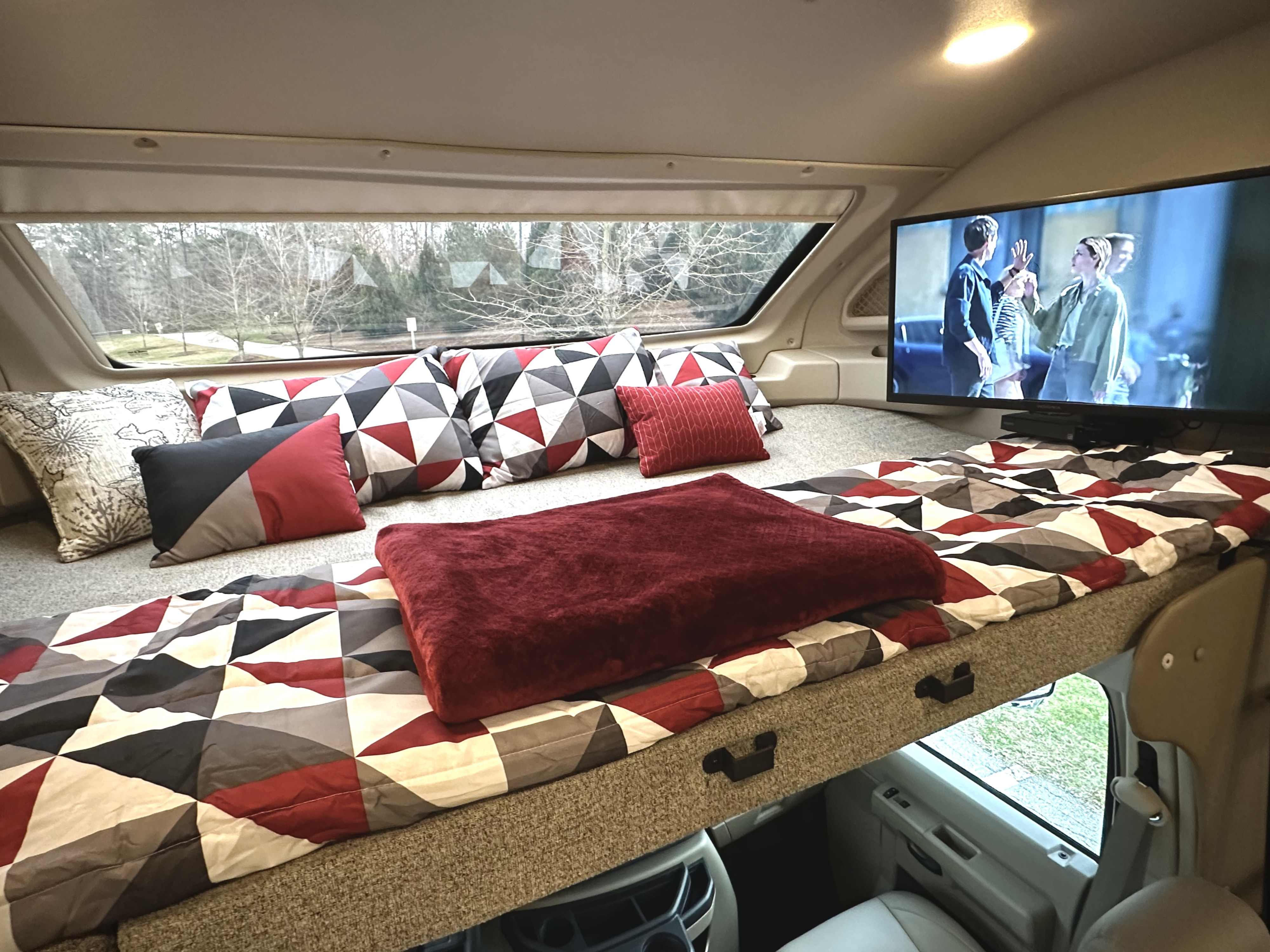 RV rental: Cab-over bunk bed with geometric bedding, red blanket, TV, and scenic window view.. Entegra Coach Esteem 2021