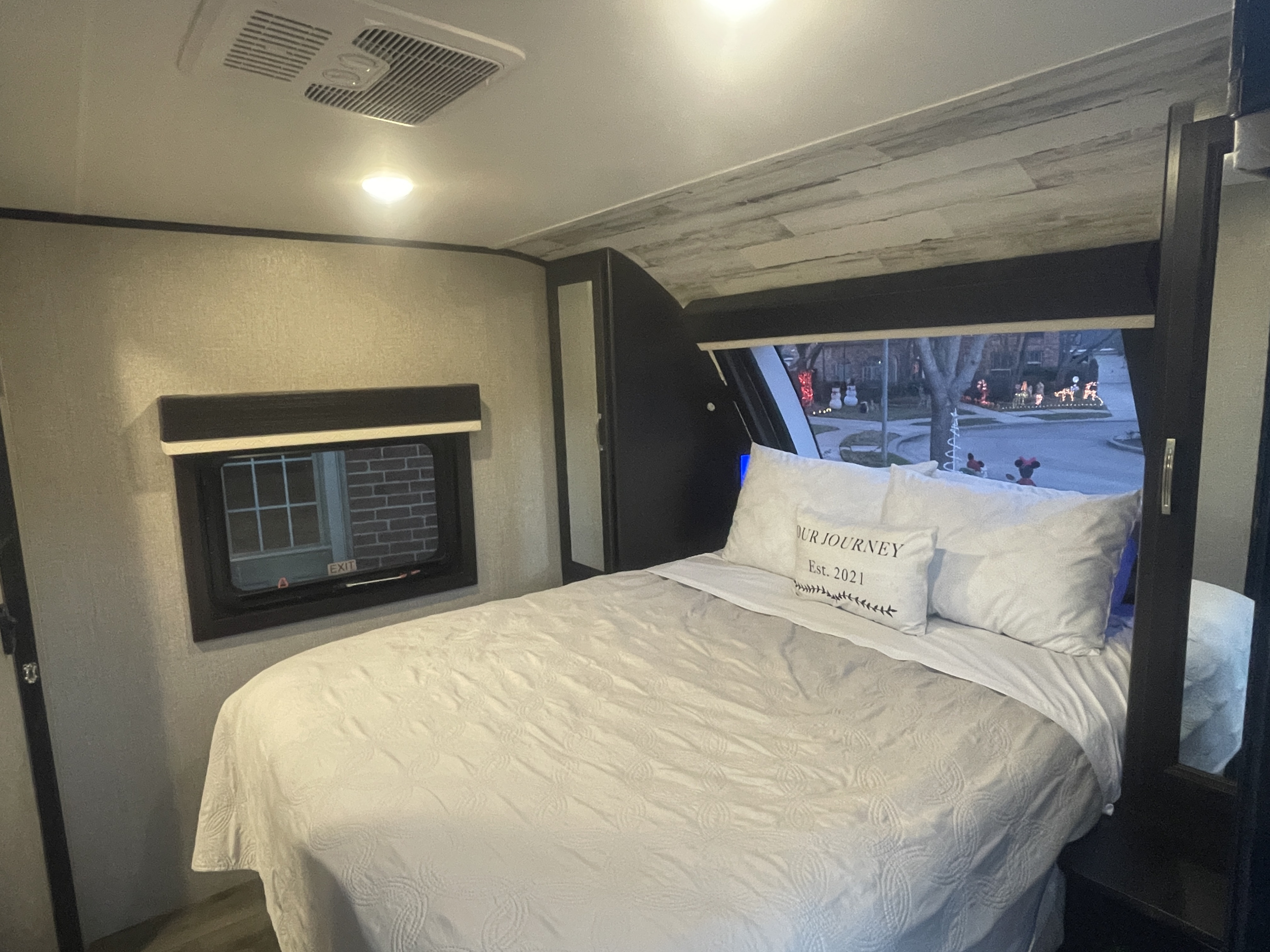 Cozy RV rental bedroom featuring a comfy bed, unique patterned ceiling, and a window view of outdoor holiday decor.. Jayco White Hawk 2021