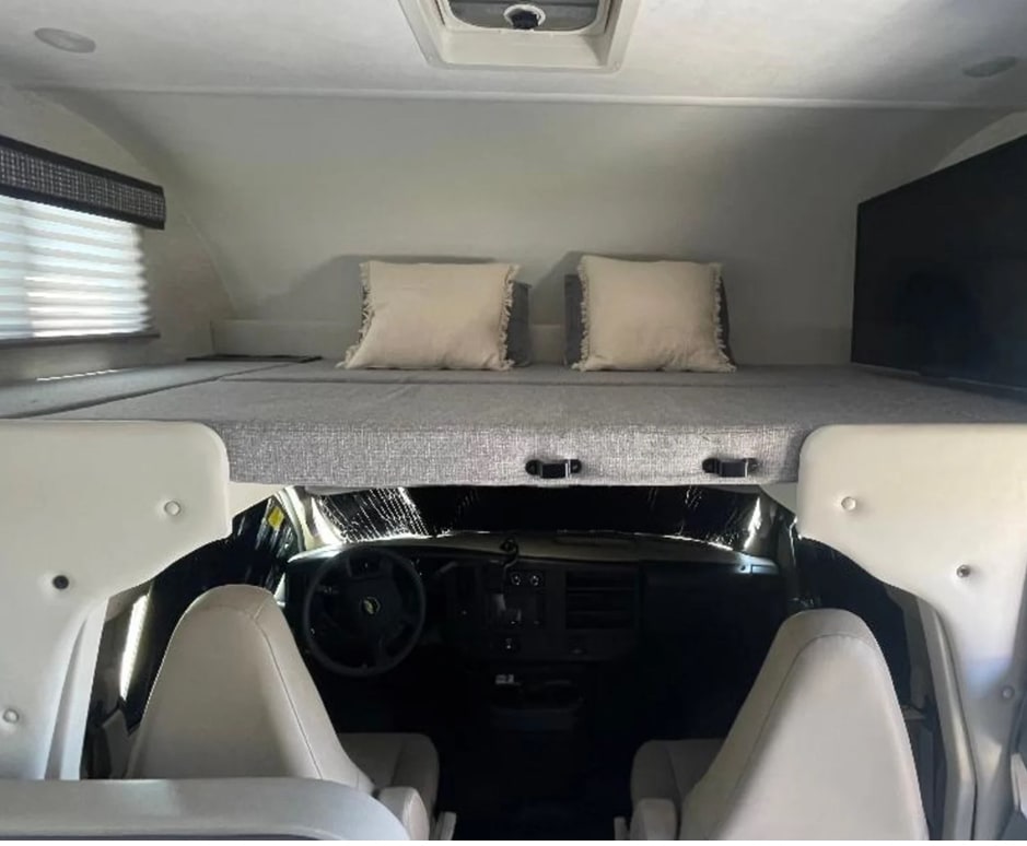 View inside an RV rental, highlighting the front overhead bunk bed with pillows, situated above the vehicle's driver cabin.. Thor Chateau 2024