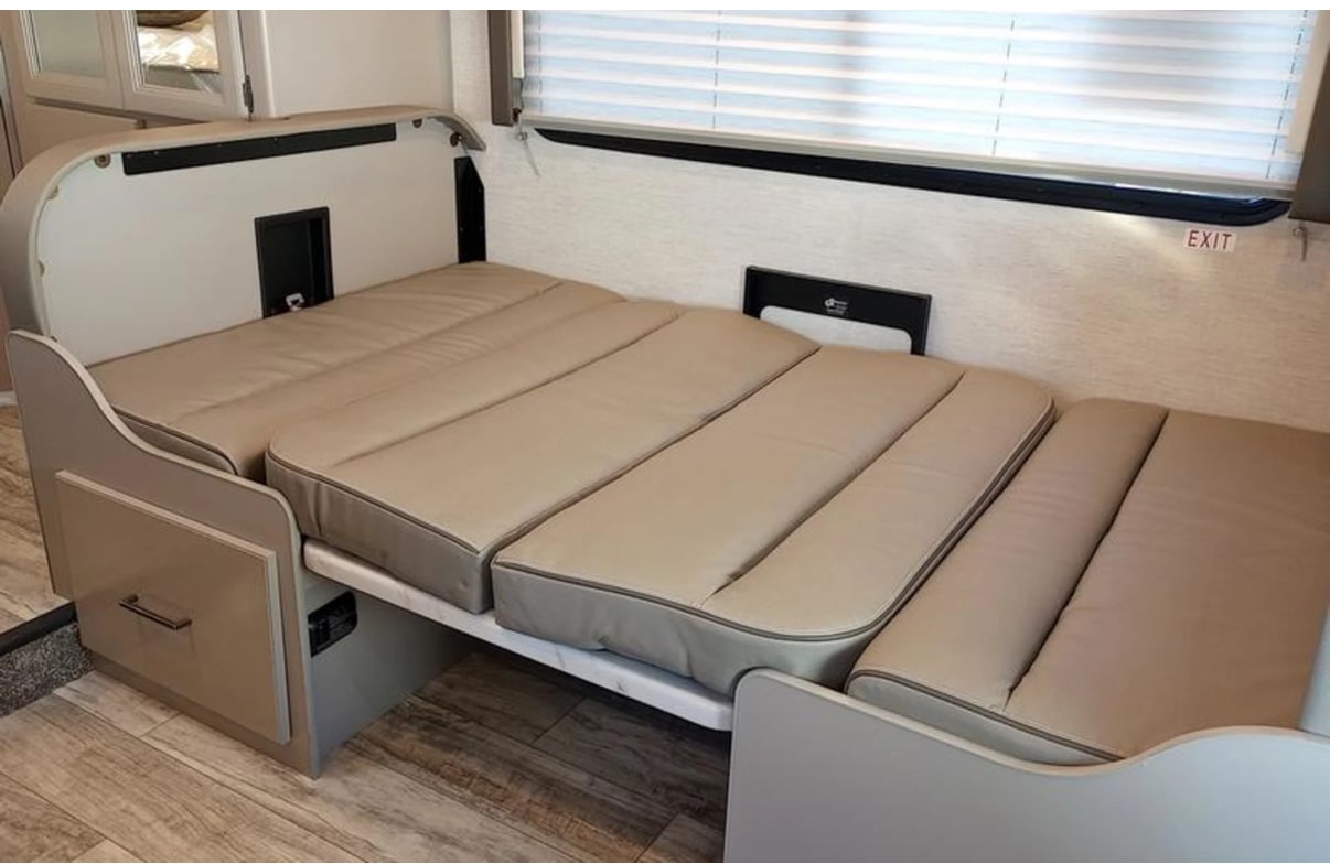 An RV rental interior reveals a light-tan, cushioned dinette converted into a bed, offering flexible space for travel.. Thor Chateau 2024