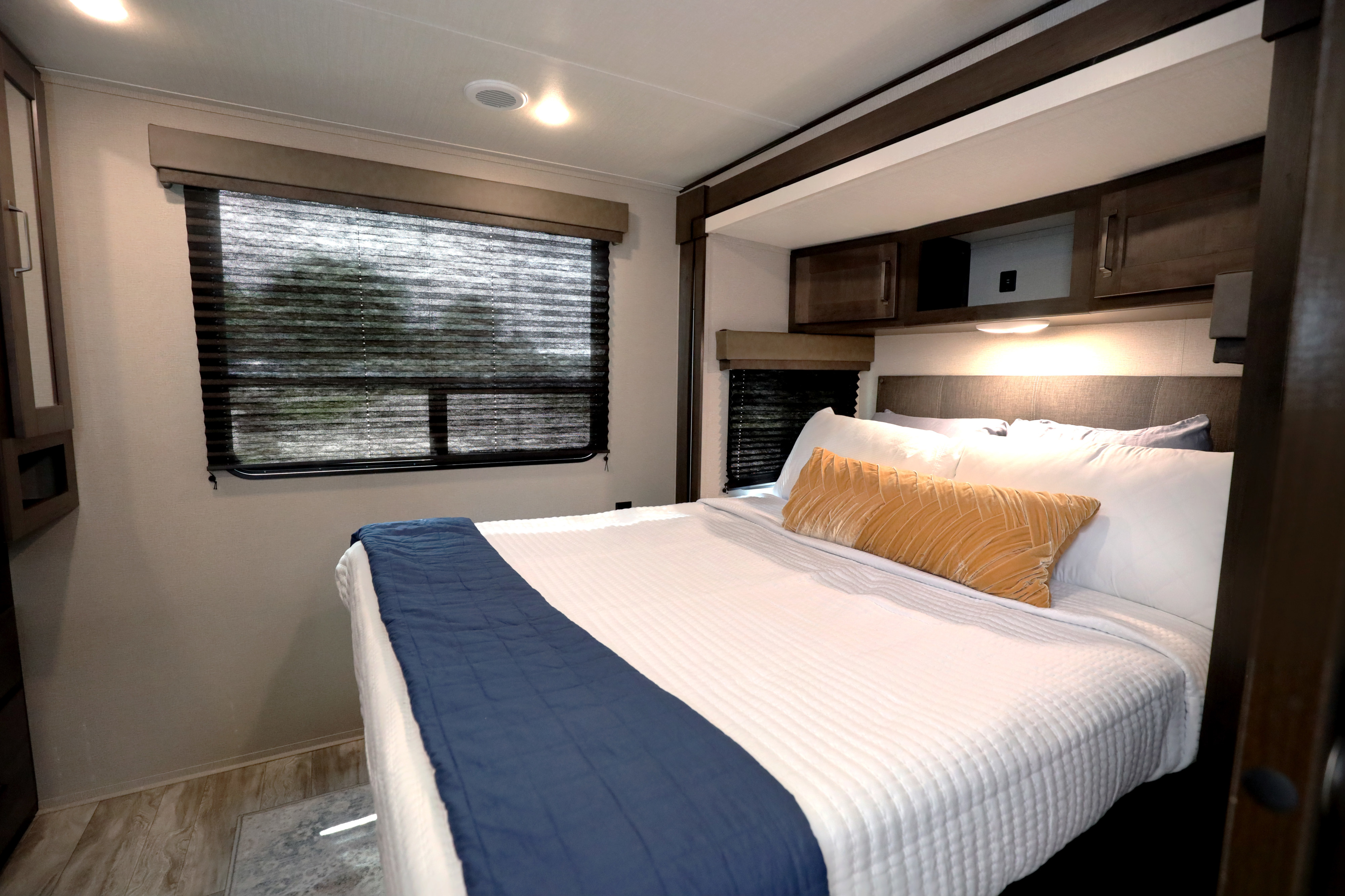 Bright RV rental bedroom showcasing a comfortable bed with a blue throw, ample storage, and window blinds for privacy.. Grand Design Transcend Xplor 2022