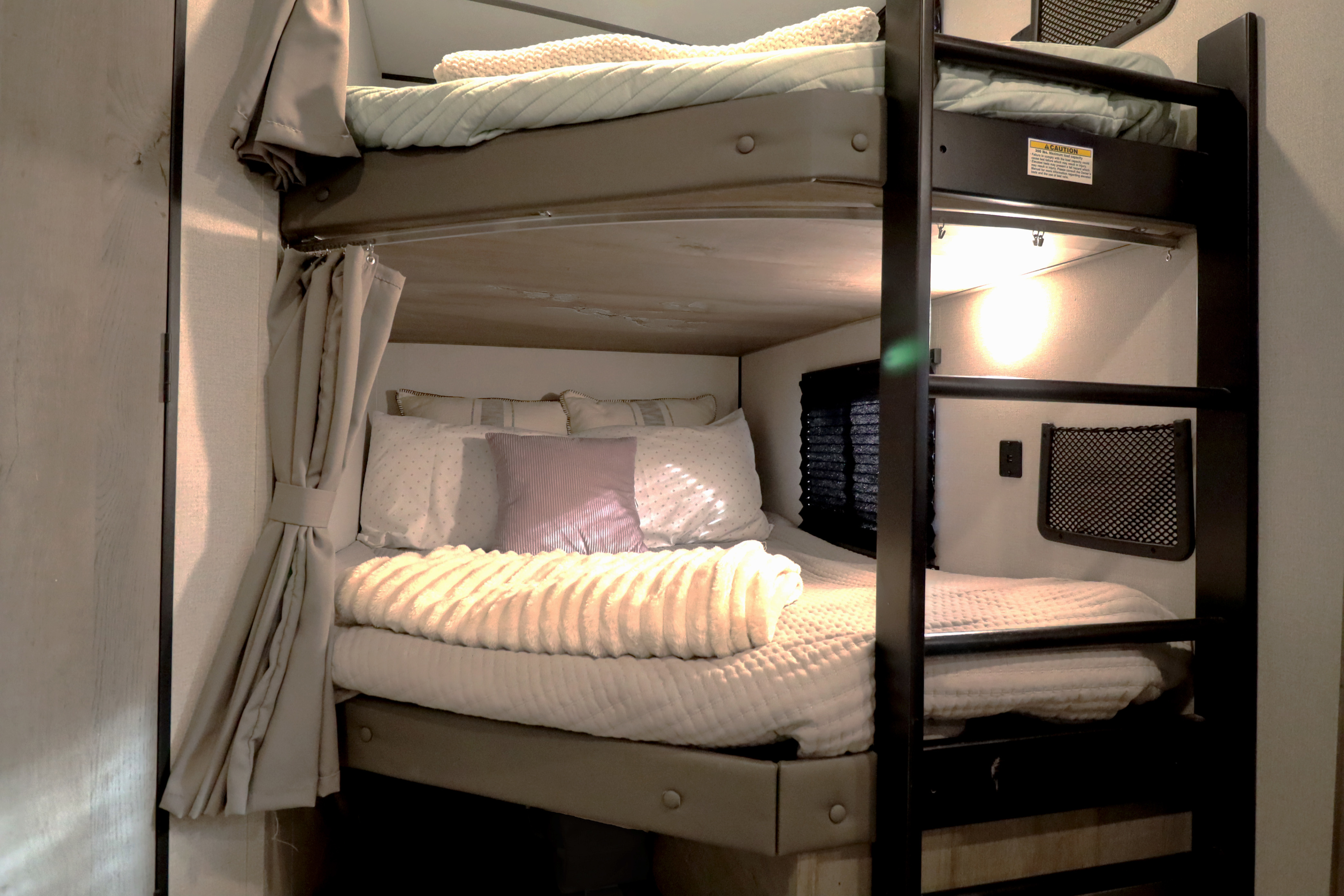 Inside a cozy RV rental, comfortable bunk beds are ready with soft bedding, pillows, and ambient lighting.. Keystone RV Springdale 2021