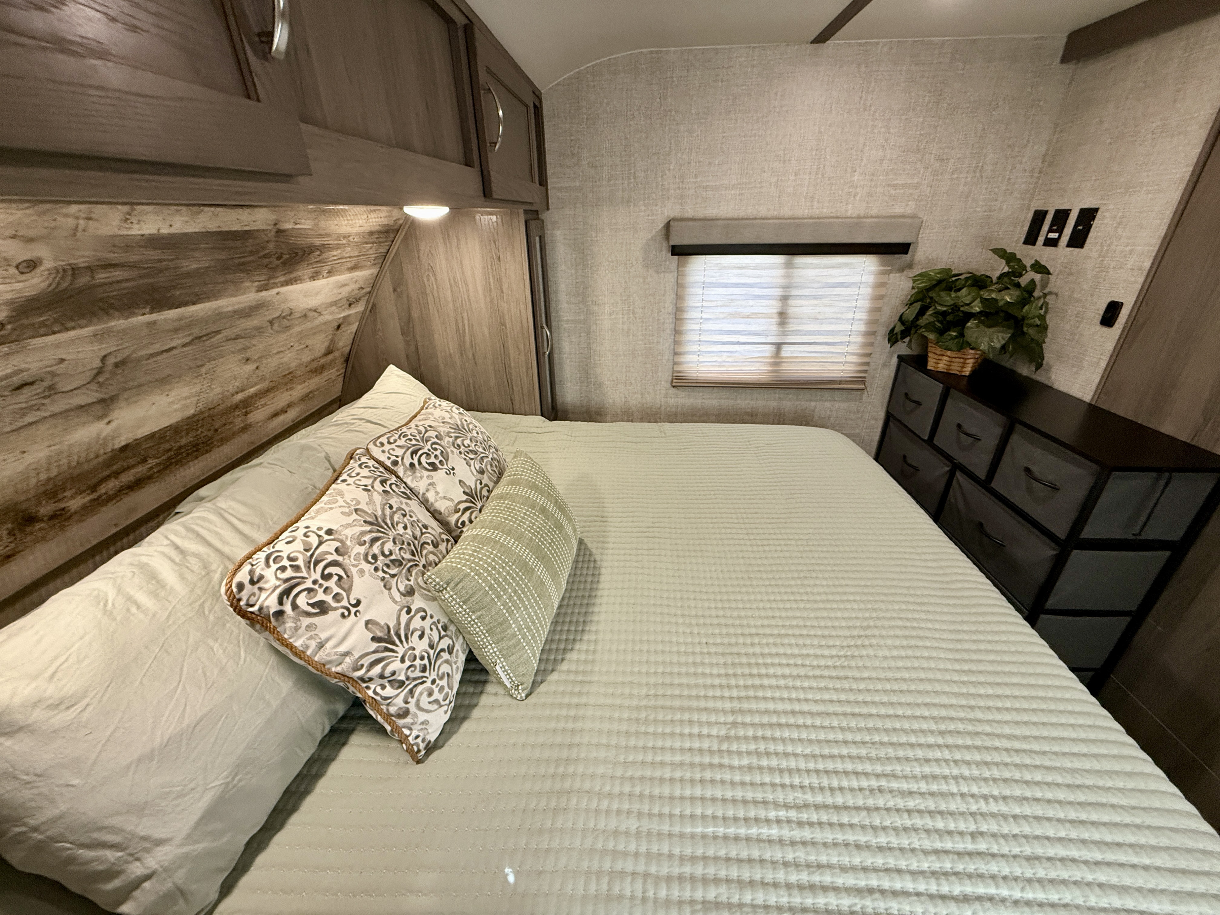 Cozy RV rental bedroom with light green bedding, wood accents, overhead cabinets, and a window for comfortable travel.. Gulf Stream Envision 2021