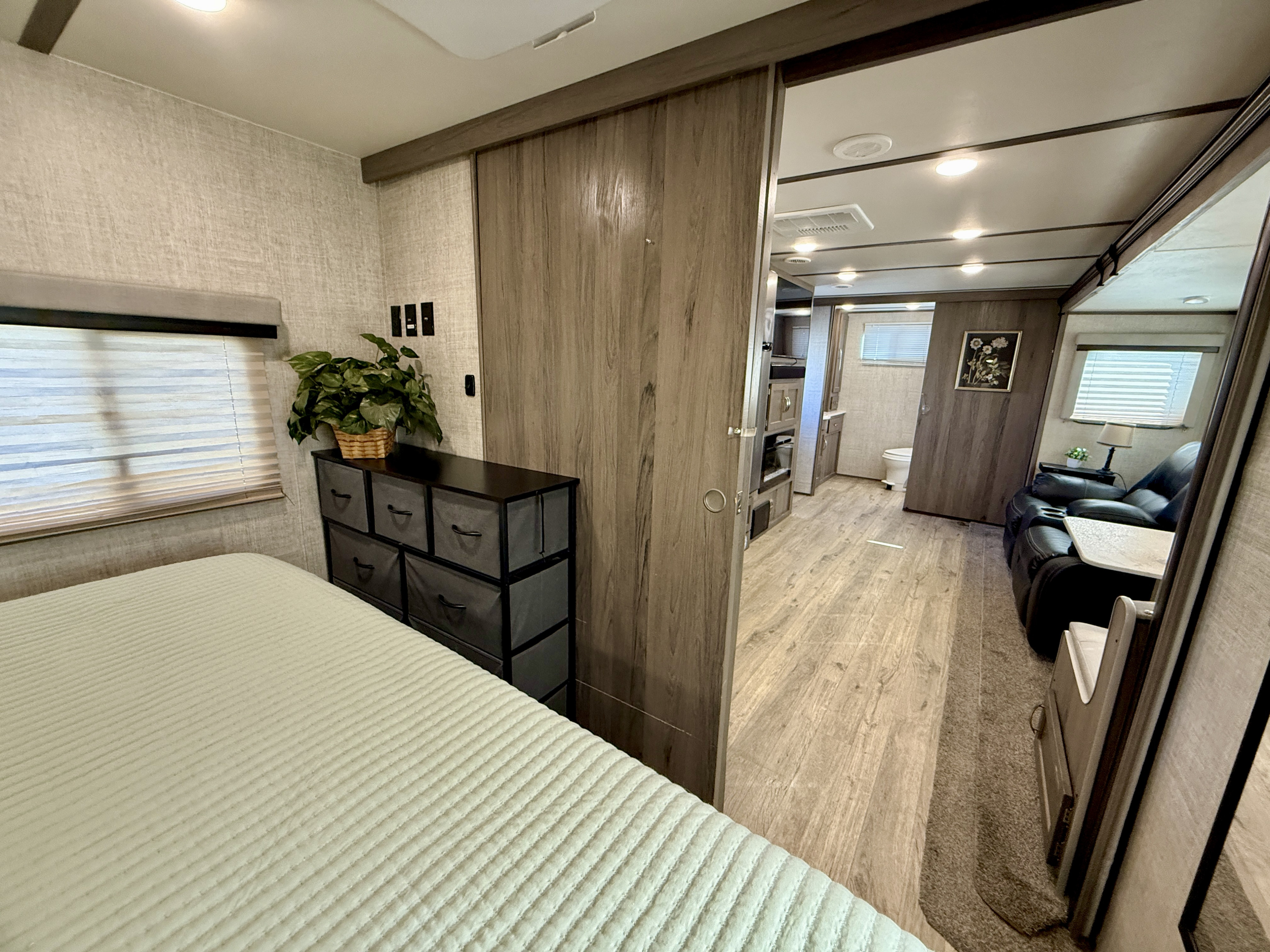 Modern RV rental interior showing the bedroom with bed and dresser, looking past a sliding door to the living area and bathroom.. Gulf Stream Envision 2021