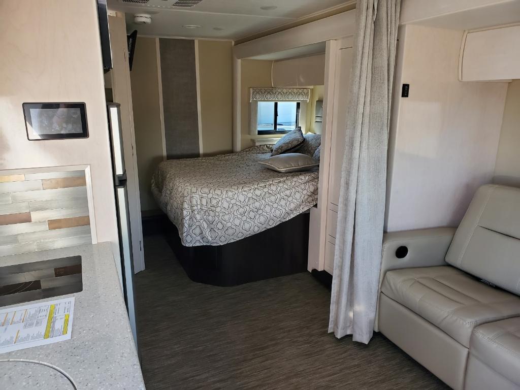 Inside an rv rental, a bedroom with a bed and window, a compact kitchen counter, and a comfortable recliner.. Renegade Custom Coaches Vienna 2021