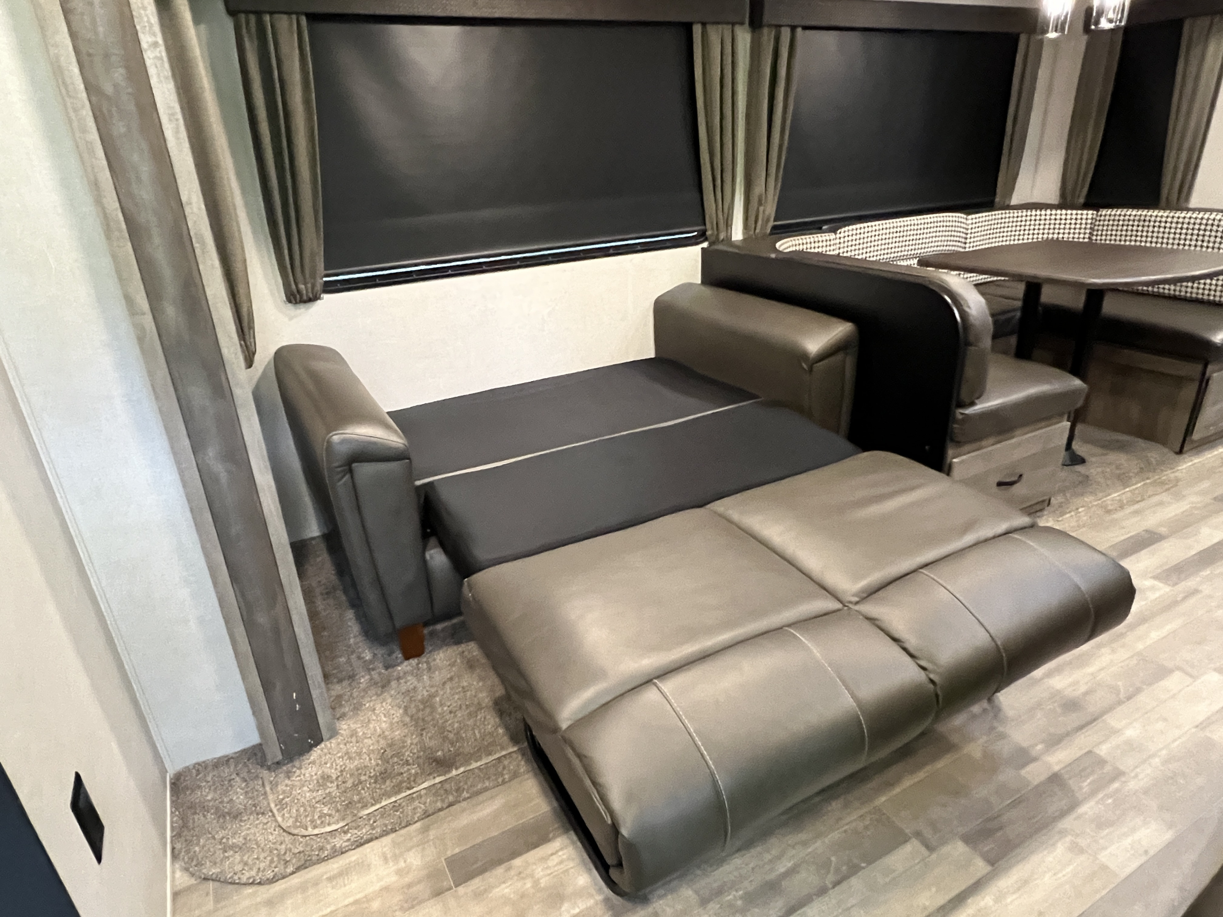 RV rental interior: A gray pull-out sofa bed in the foreground, with a black and white checkered dinette.. Forest River Vibe 2020
