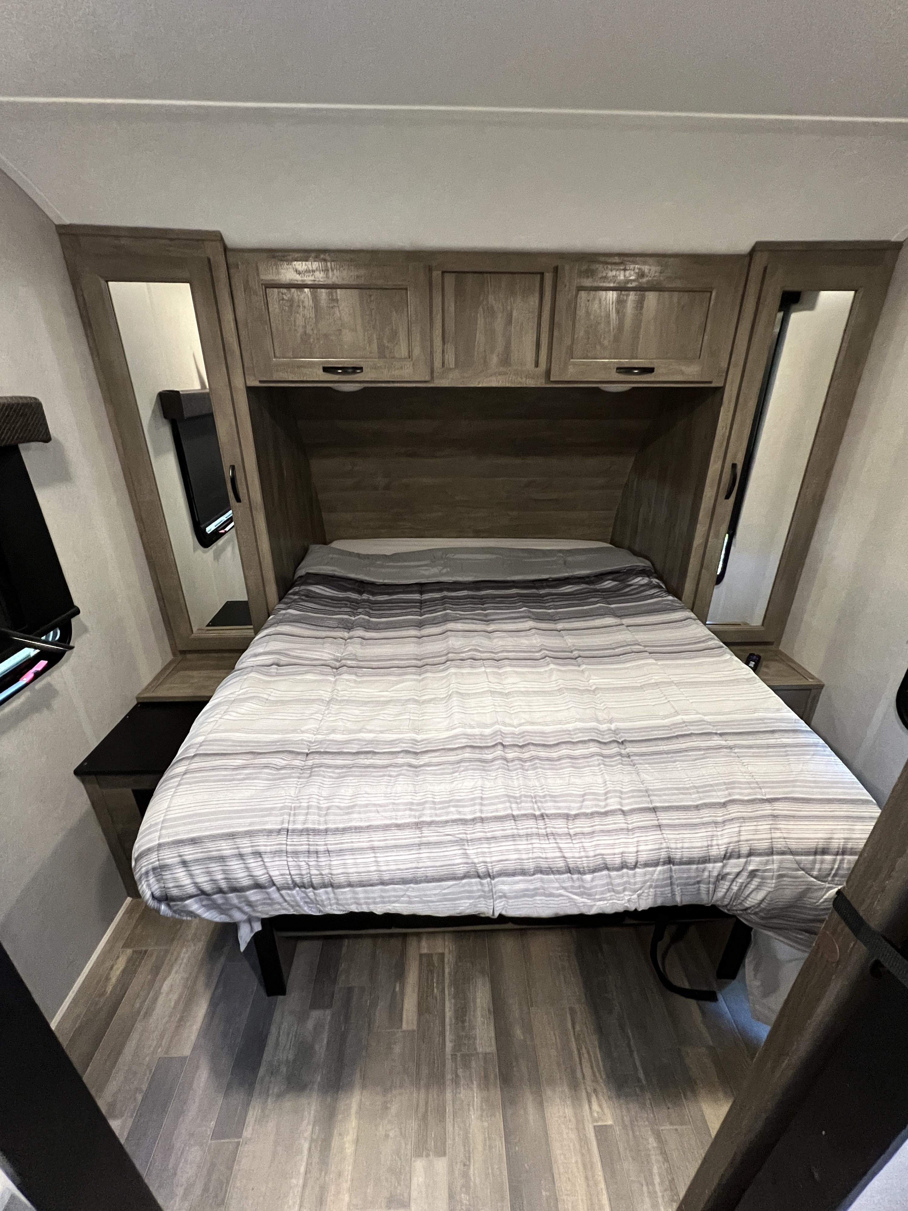 RV rental bedroom: cozy interior with striped bed, overhead cabinets, and mirrored storage on both sides.. Forest River Vibe 2020