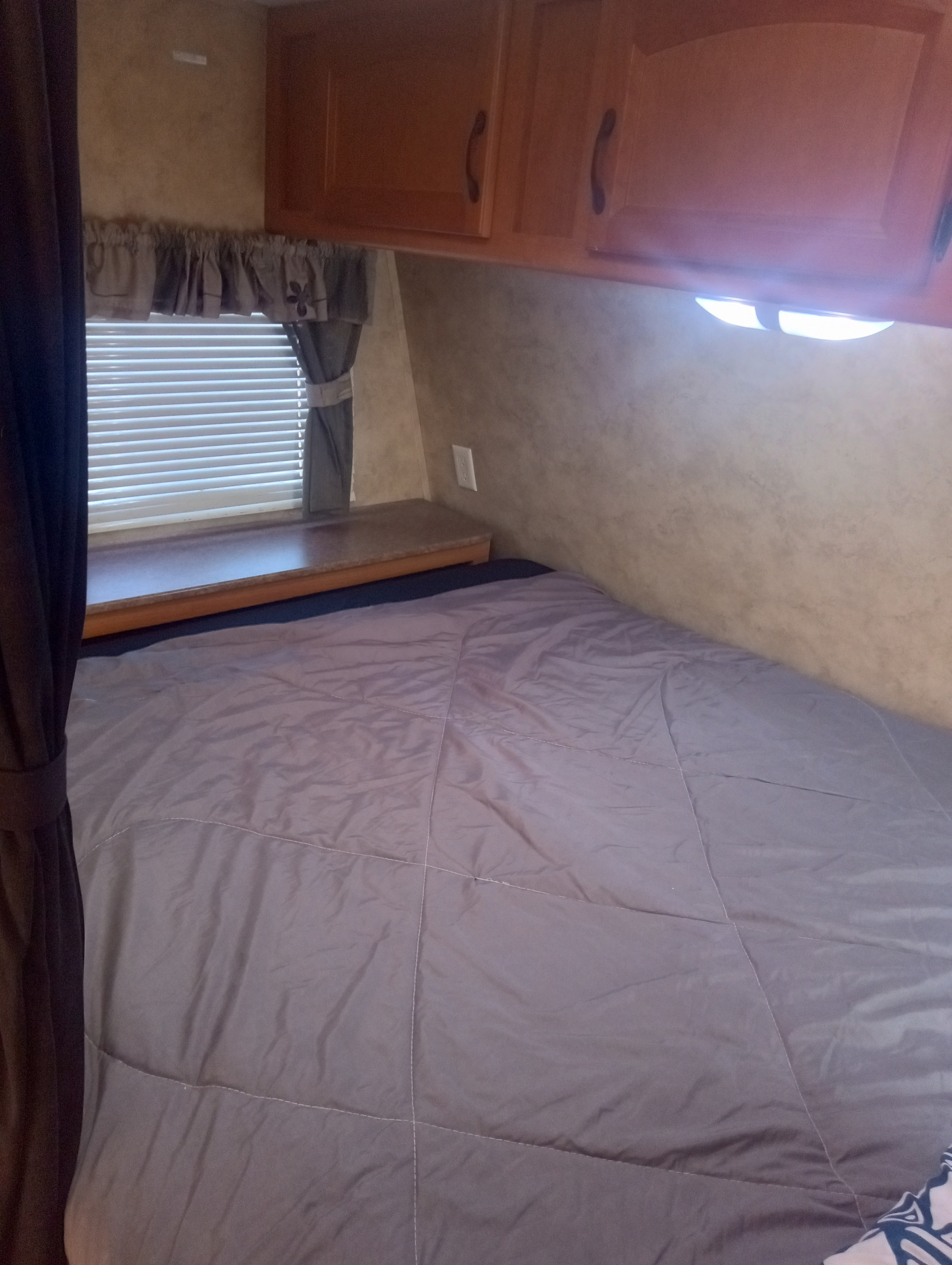 Cozy RV rental bedroom featuring a comfortable bed, window with blinds, and practical overhead cabinets.. Keystone Energy 2010