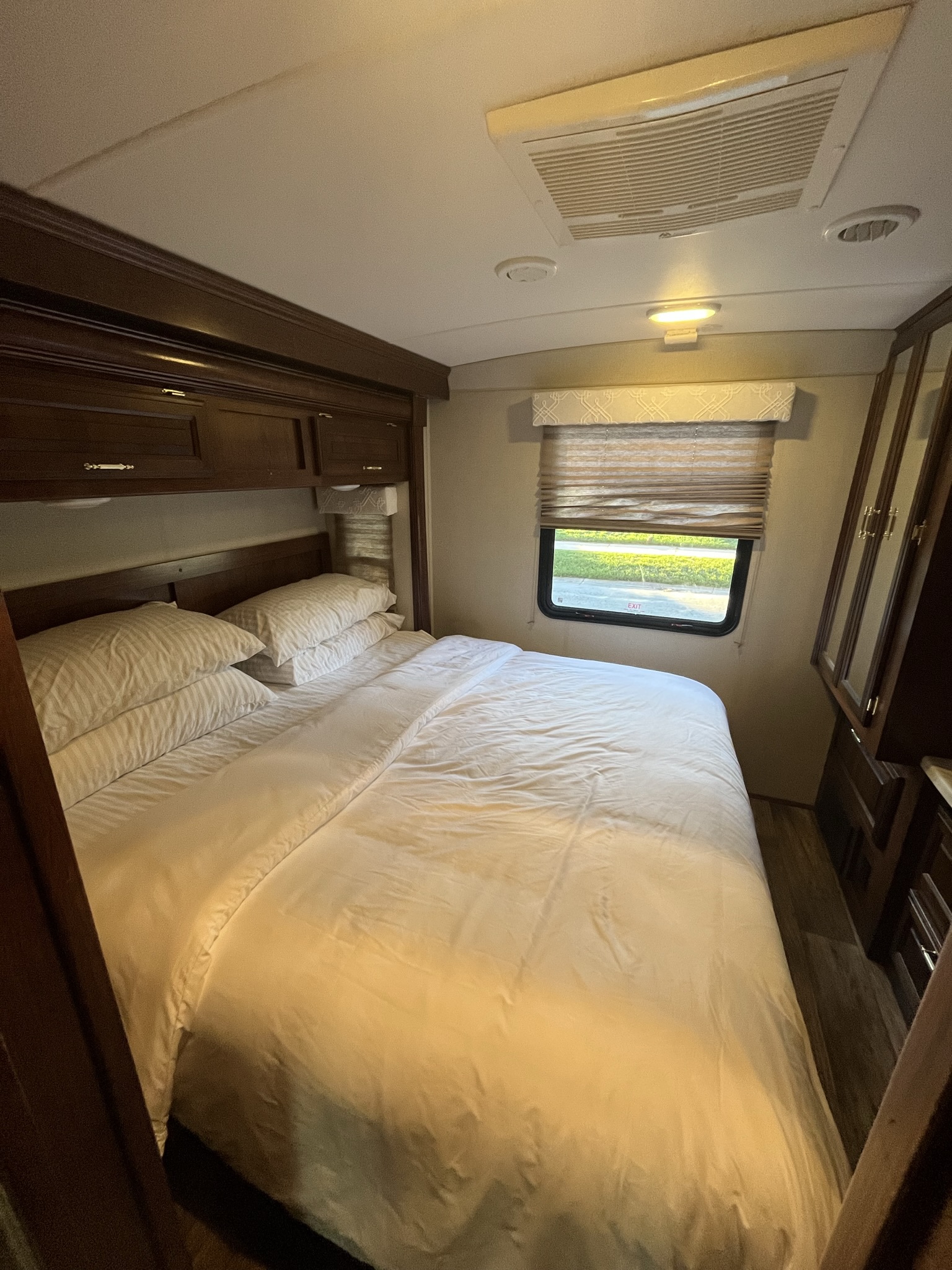 Cozy RV rental bedroom features a comfy white bed, dark wood storage, a window, and overhead AC, perfect for travel.. FR3 FR3 Motorhome 2018