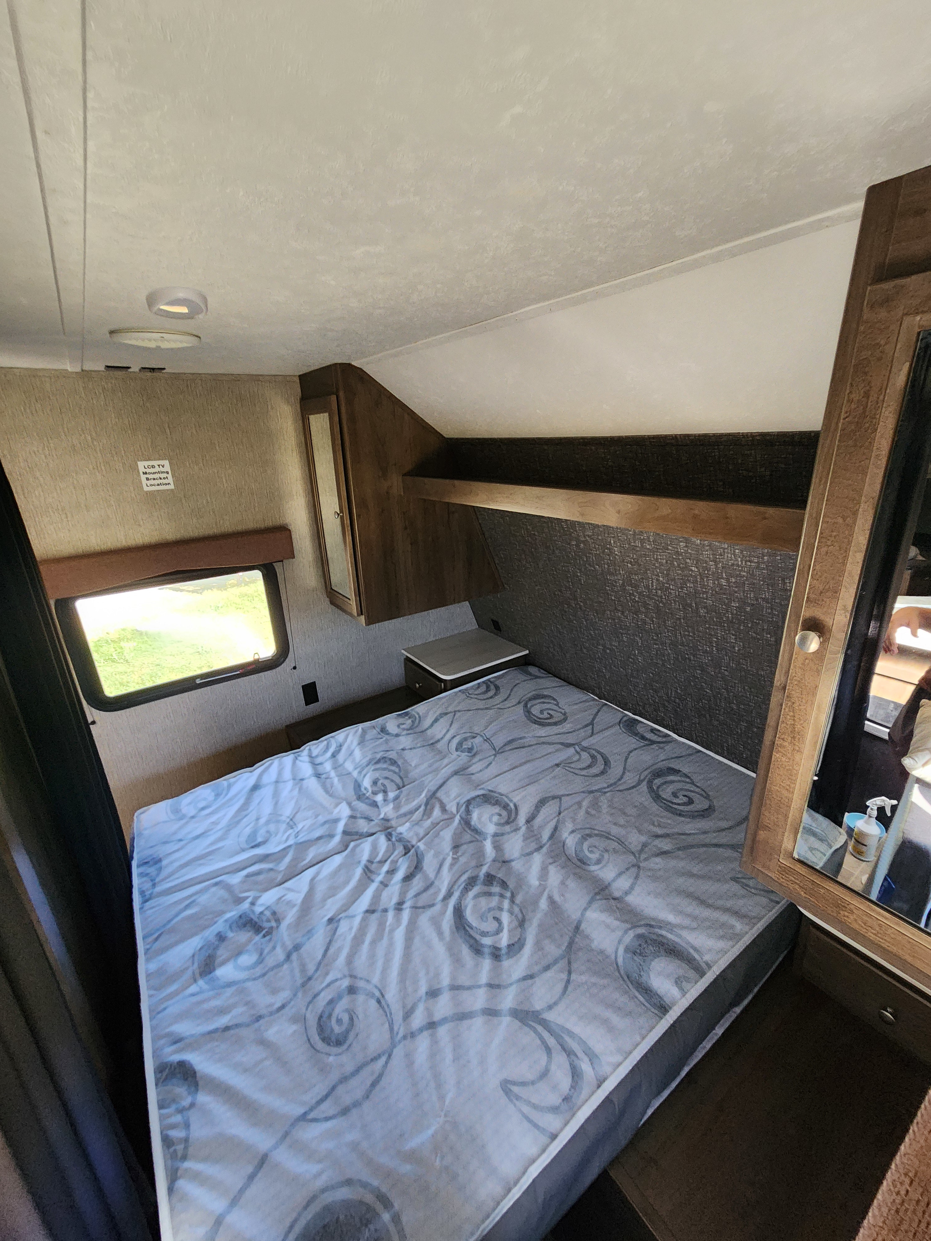 Compact RV rental bedroom with a patterned mattress, window, and built-in storage, showcasing a practical travel trailer interior.. Dutchmen Coleman Lantern 2019