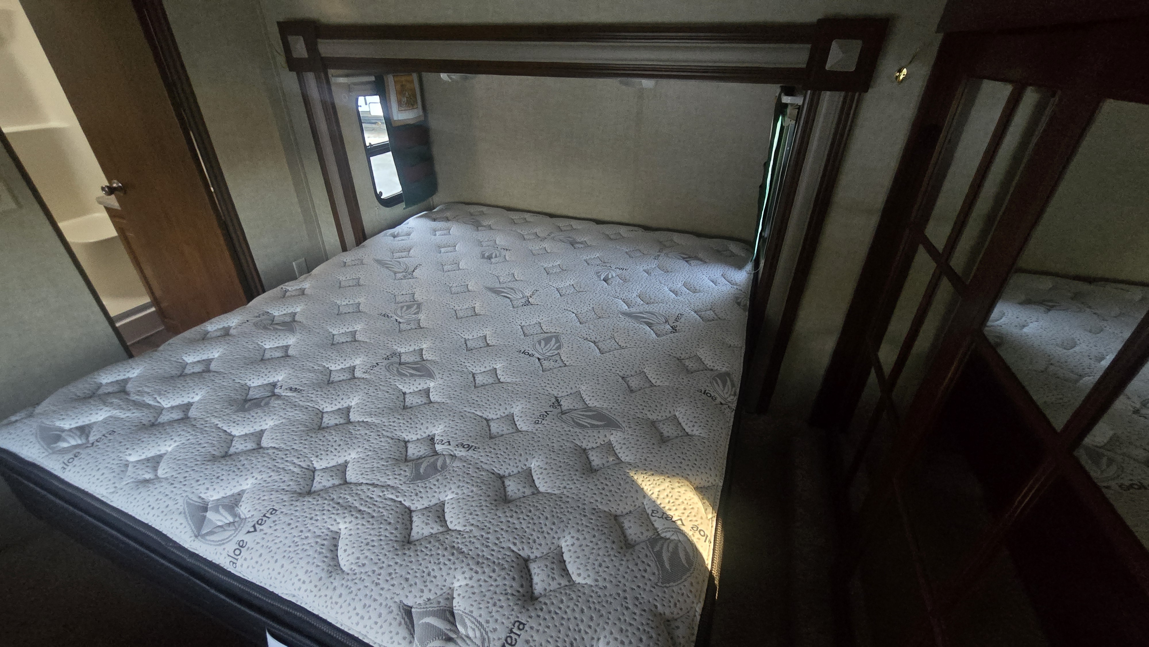 Compact RV rental bedroom with an "aloe vera" mattress, window, and mirrored wardrobe, ideal for travel.. Keystone Laredo 2013