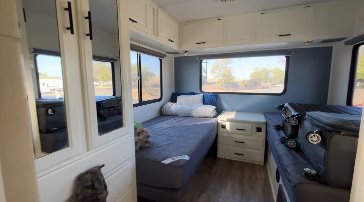 RV rental interior: A compact bedroom features two beds, a nightstand, overhead cabinets, and large windows with outdoor views.. Four Winds Windsport 2001
