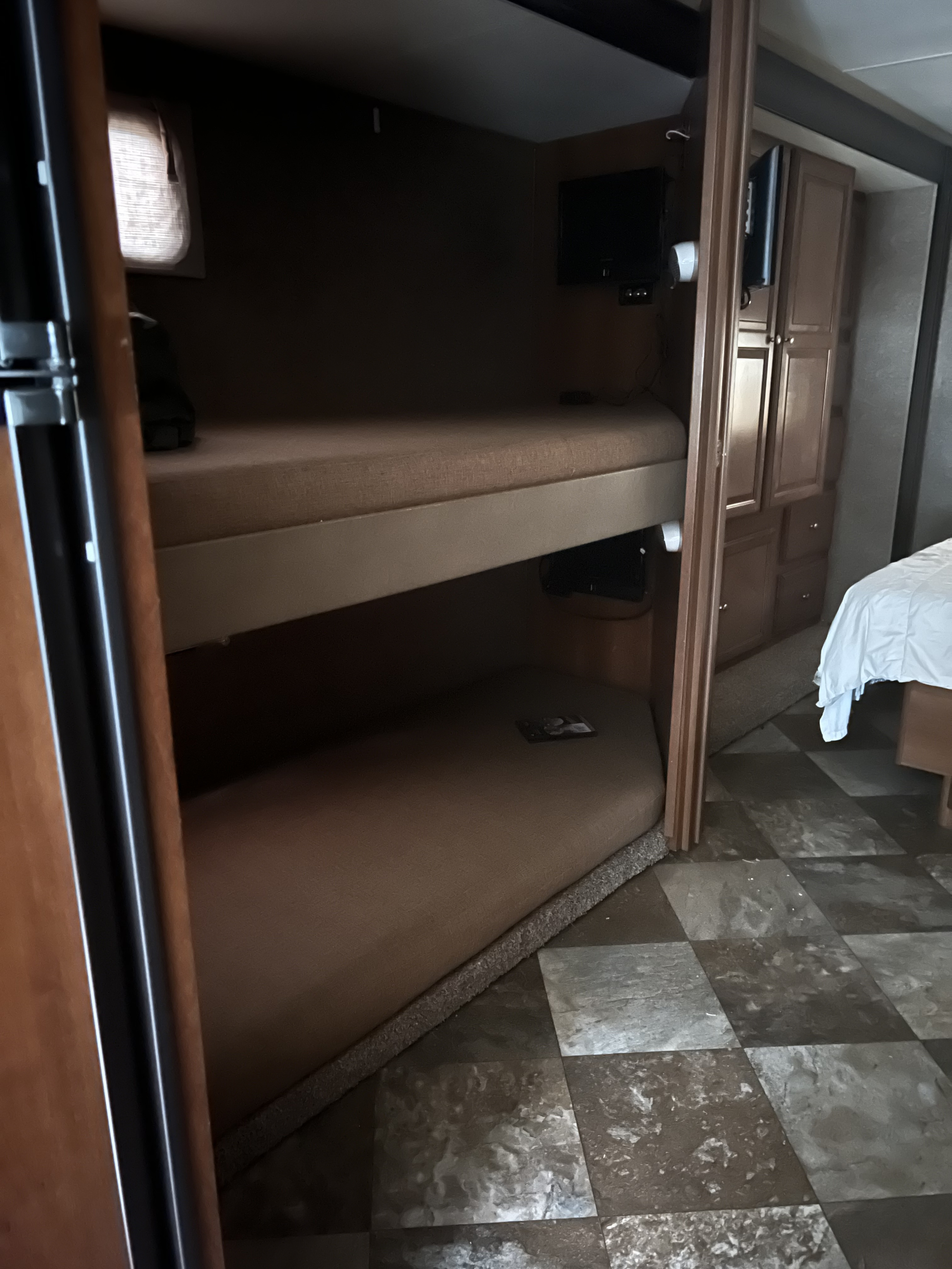 An RV rental interior features two built-in bunk beds with TVs, wood cabinets, and a partial view of another bed.. Coachmen Leprechaun 2015
