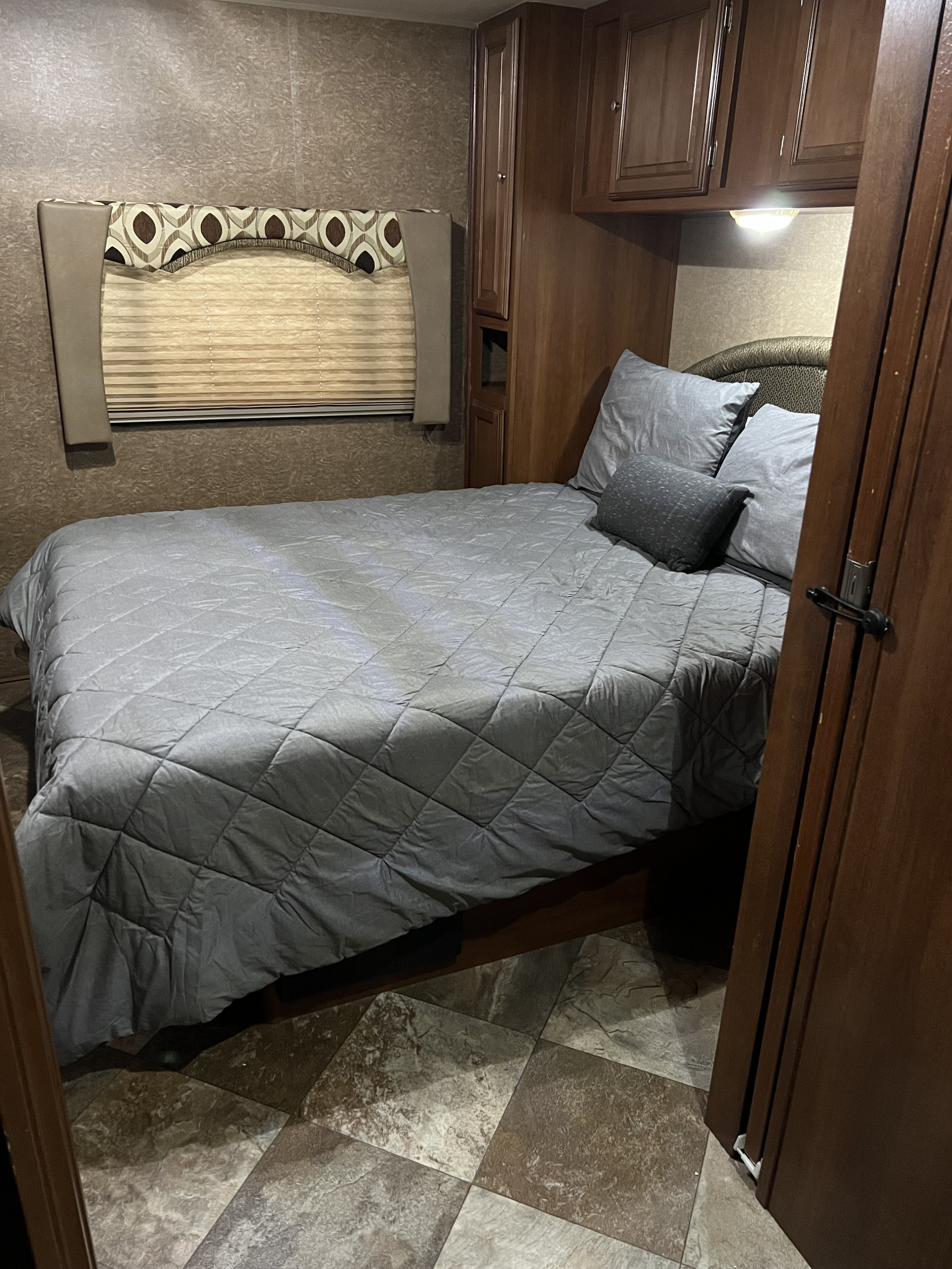 Cozy RV rental bedroom with gray bedding, built-in cabinets, and patterned window treatments, visible from an open doorway.. Coachmen Leprechaun 2015