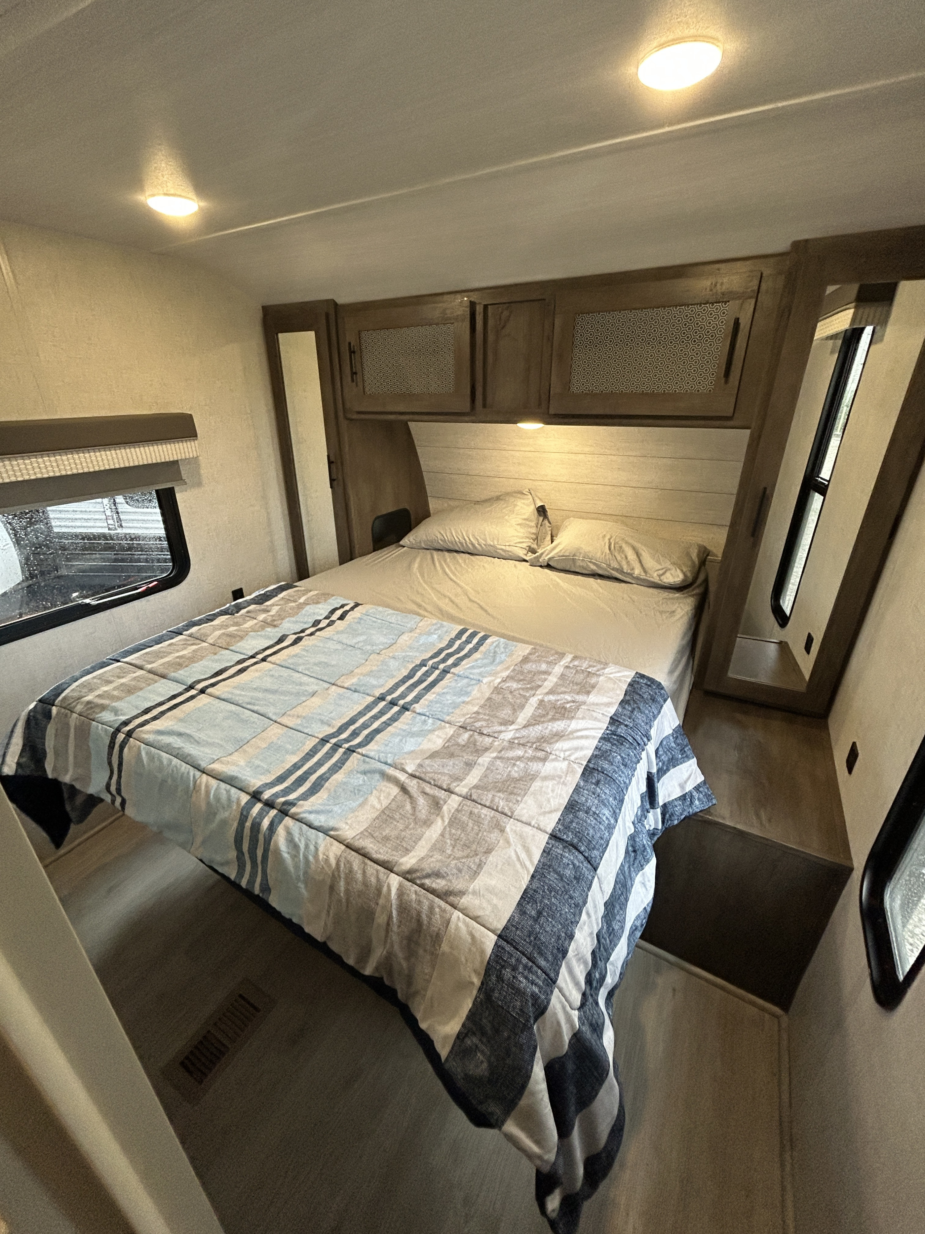 Compact, cozy RV rental bedroom features a striped comforter, overhead storage, and window, perfect for travel comfort.. Forest River Salem 2021