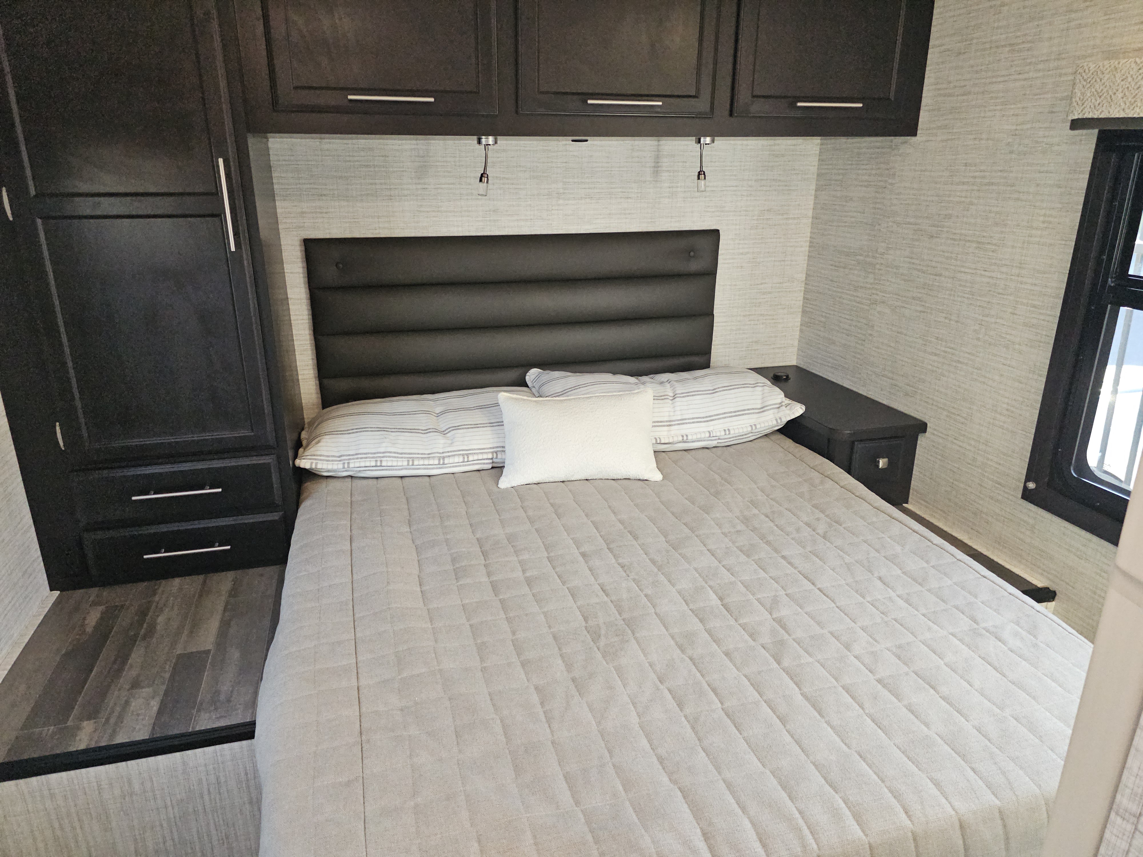 Cozy RV rental bedroom featuring a queen bed, upholstered headboard, and dark wood storage cabinets. Ideal for travel.. Jayco Redhawk 2024