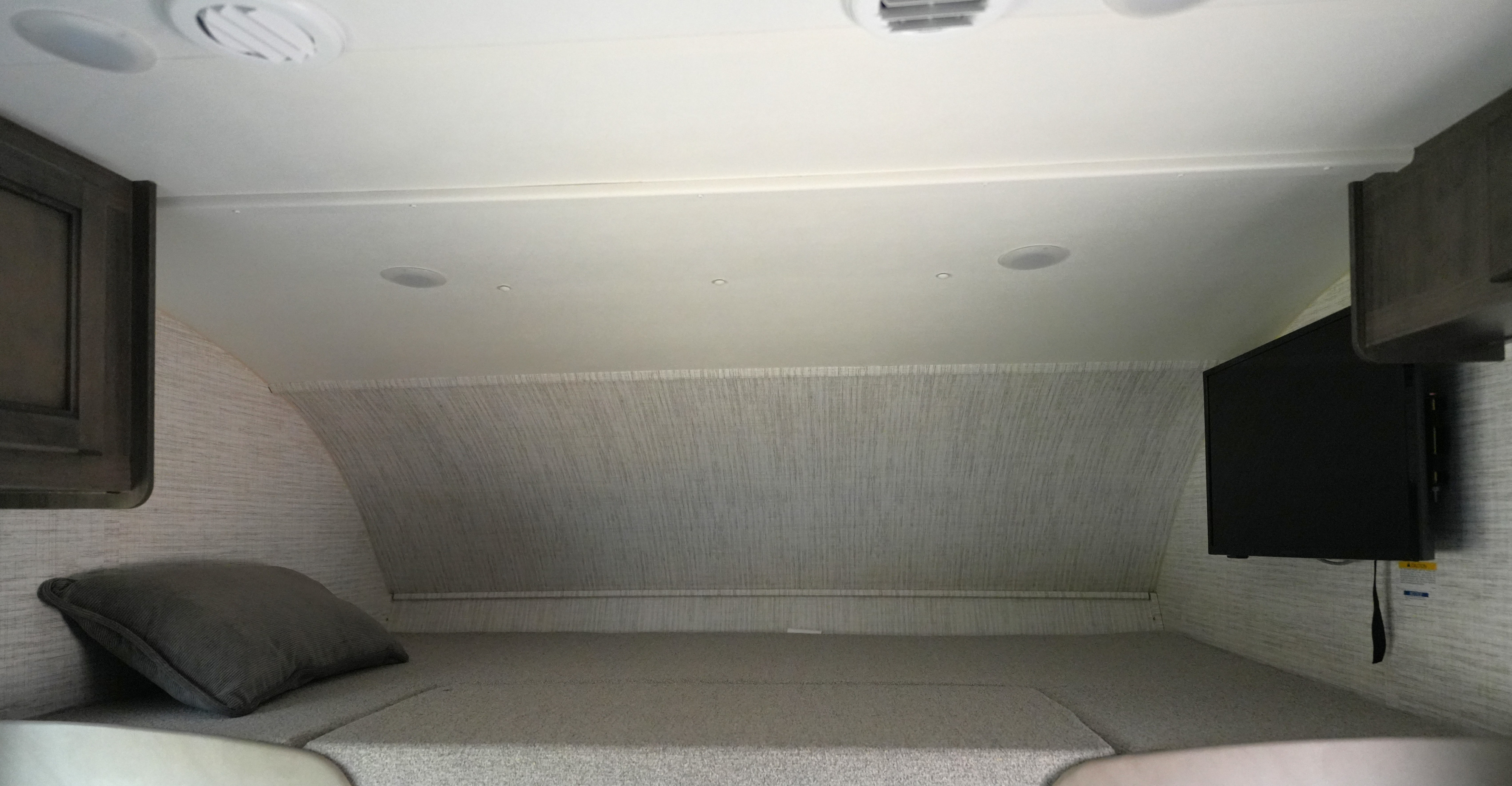 Interior of an RV rental: cozy overhead bunk area with a bed, mounted TV, ceiling lights, and textured walls.. Jayco Redhawk SE 2024