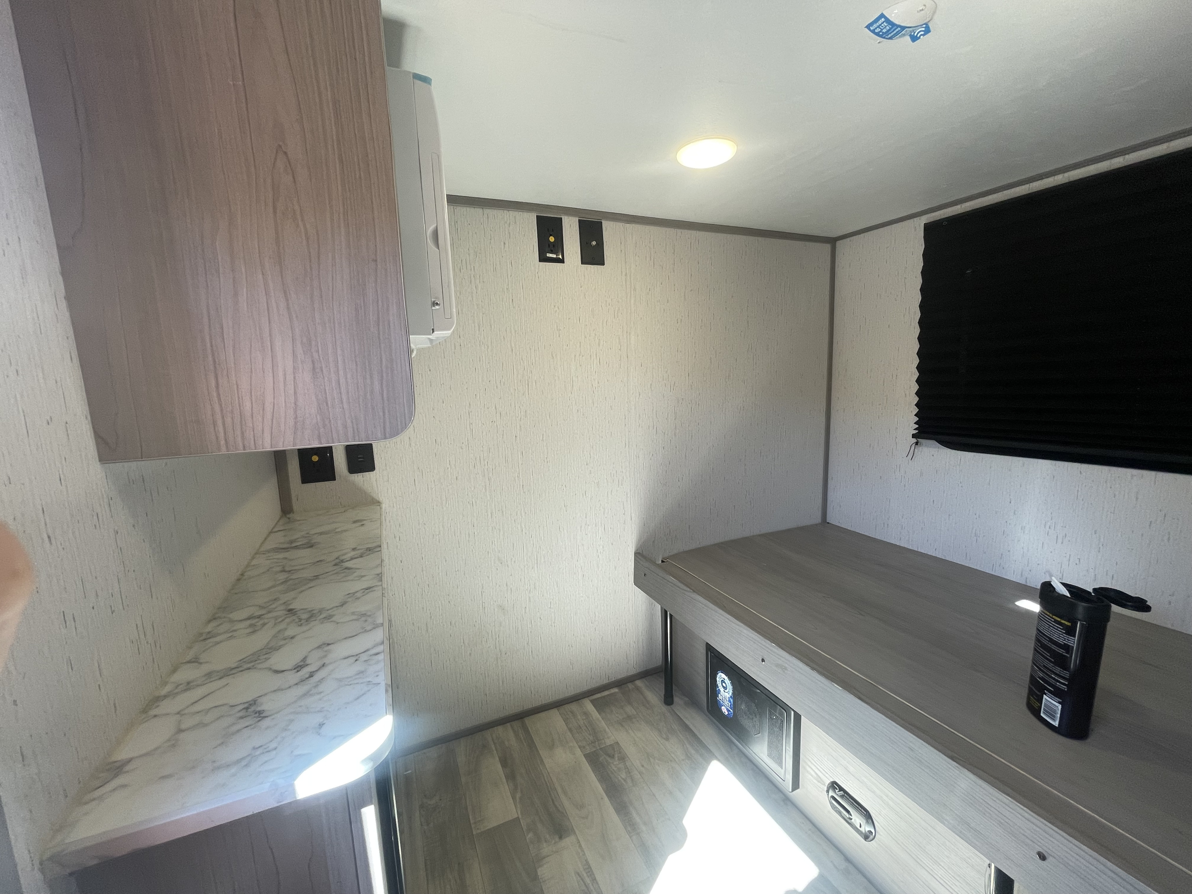 Bright RV rental interior showing a sleeping/lounge area with wood-look floor, countertop, and a built-in bunk/bed. Includes AC unit & outlets.. Dutchmen Coleman Rubicon 2023