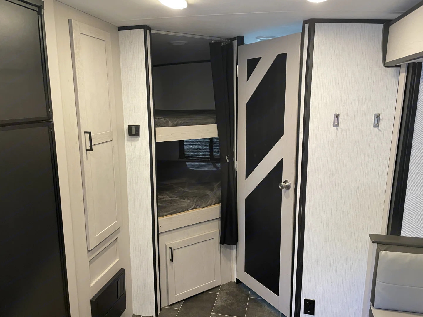 Inside an RV rental: a modern interior with light-colored cabinets, bunk beds, and a patterned door leading to another area.. Heartland RVs Mallard 2022
