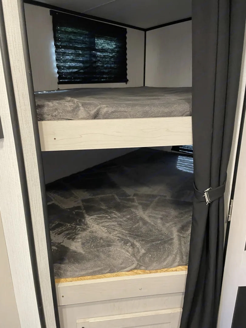 RV rental: Compact bunk beds with grey bedding, a window with blinds, and a side privacy curtain.. Heartland RVs Mallard 2022
