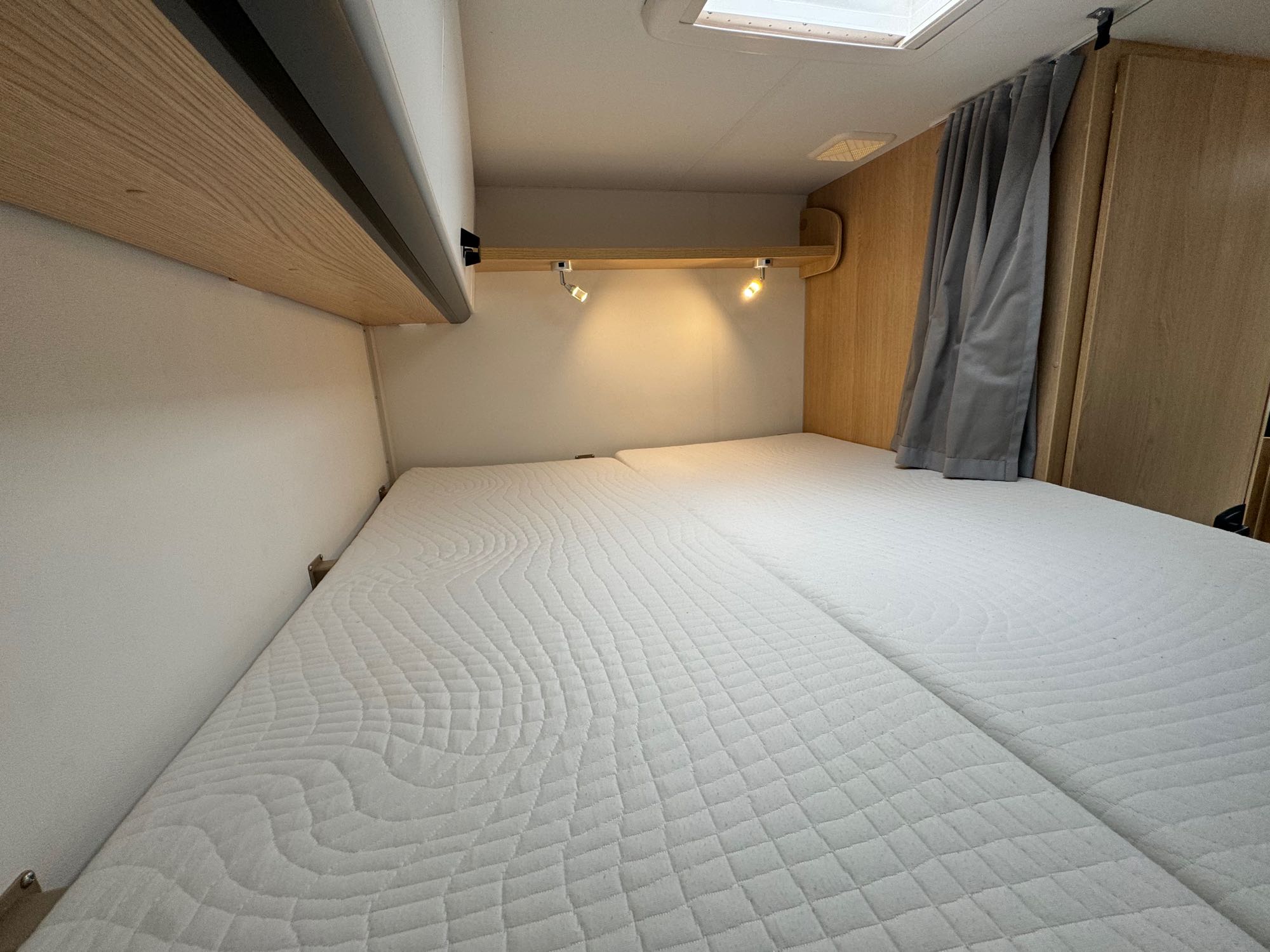Inside an RV rental: a well-lit bedroom featuring two quilted mattresses, wooden trim, and privacy curtains.. Sunlight V60 2025