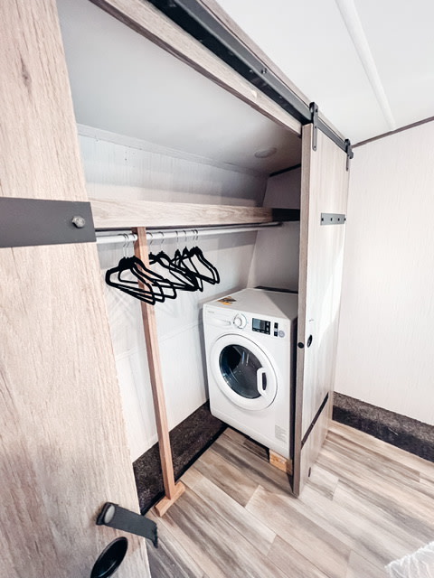 Efficient laundry setup in an RV rental: a white washing machine tucked into a closet with hangers.. Heartland RVs Milestone 2021