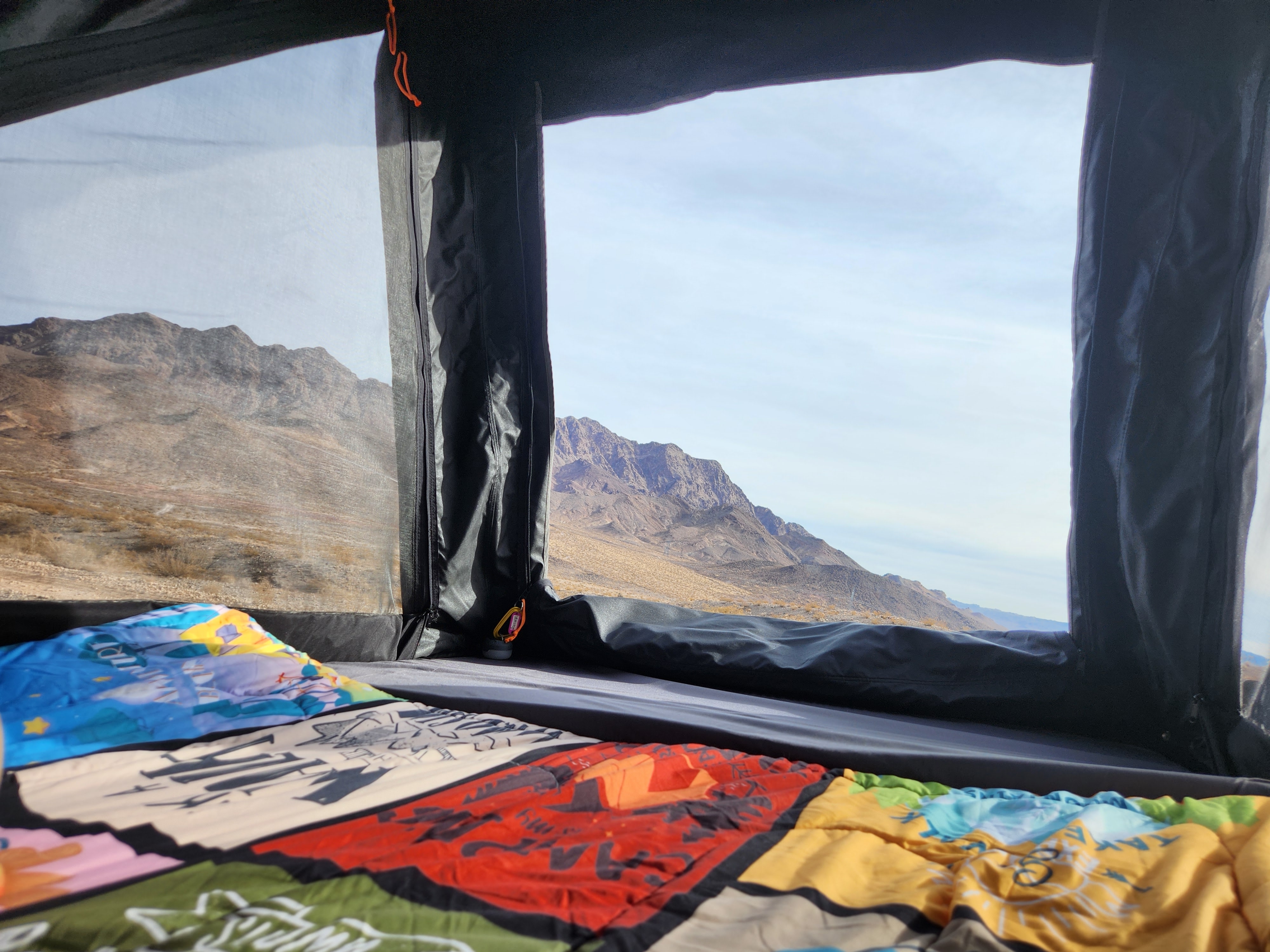 Inside an RV rental, a colorful blanket lies on the bed, offering a panoramic desert mountain view through the window.. Other Other 2021