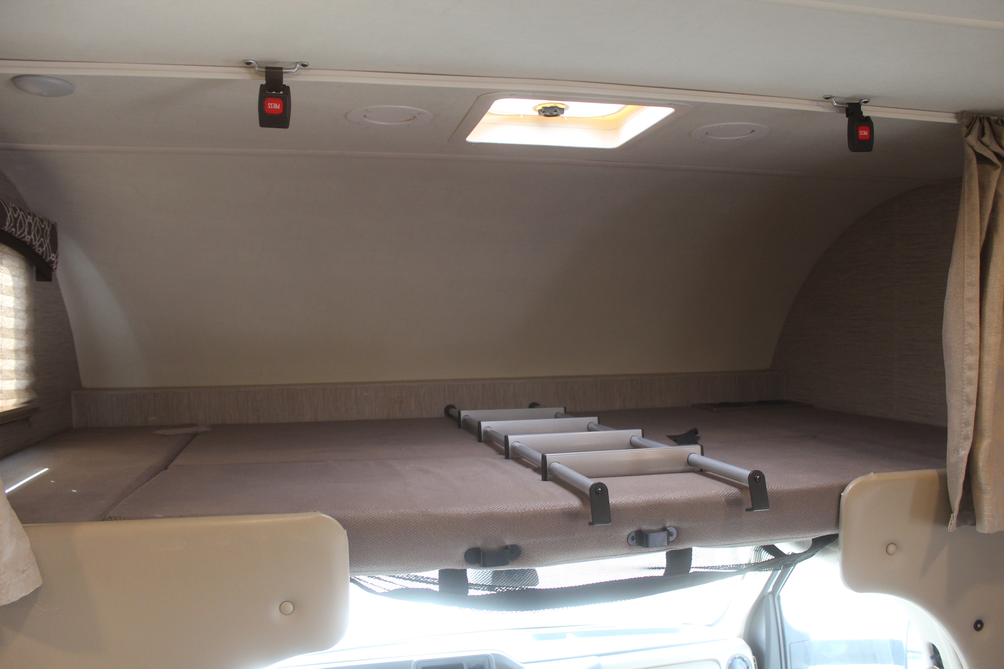 Overhead RV rental bunk bed with ladder and ceiling-mounted safety buckles, providing a sleeping area.. Thor Chateau 2021