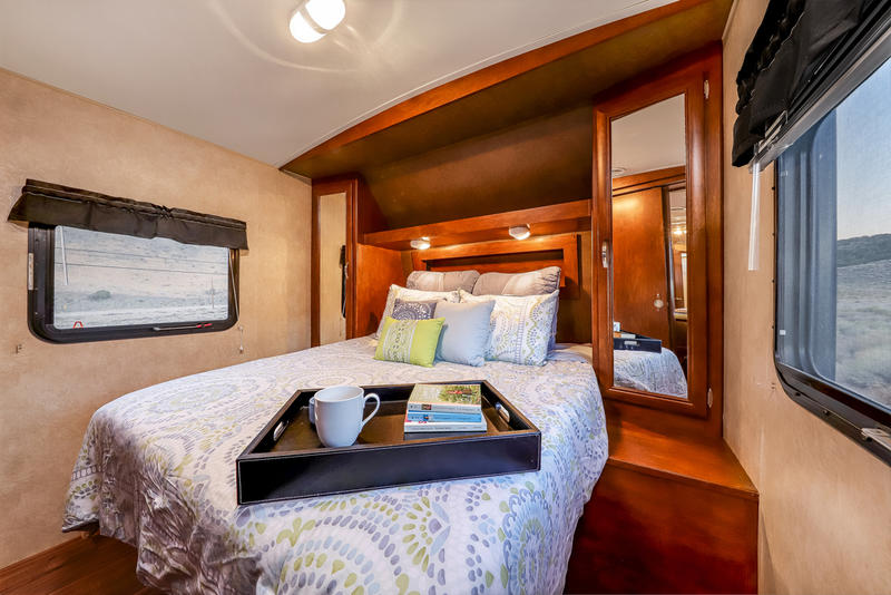 Cozy RV rental bedroom with a comfy bed, wood cabinetry, and scenic outdoor views through windows.. Forest River Vibe 2018
