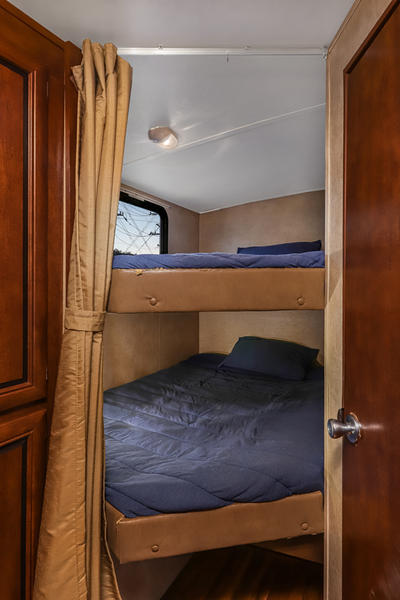 RV rental: Cozy bunk beds with blue bedding in a travel trailer's compact sleeping area, featuring a window & privacy curtain.. Forest River Vibe 2018