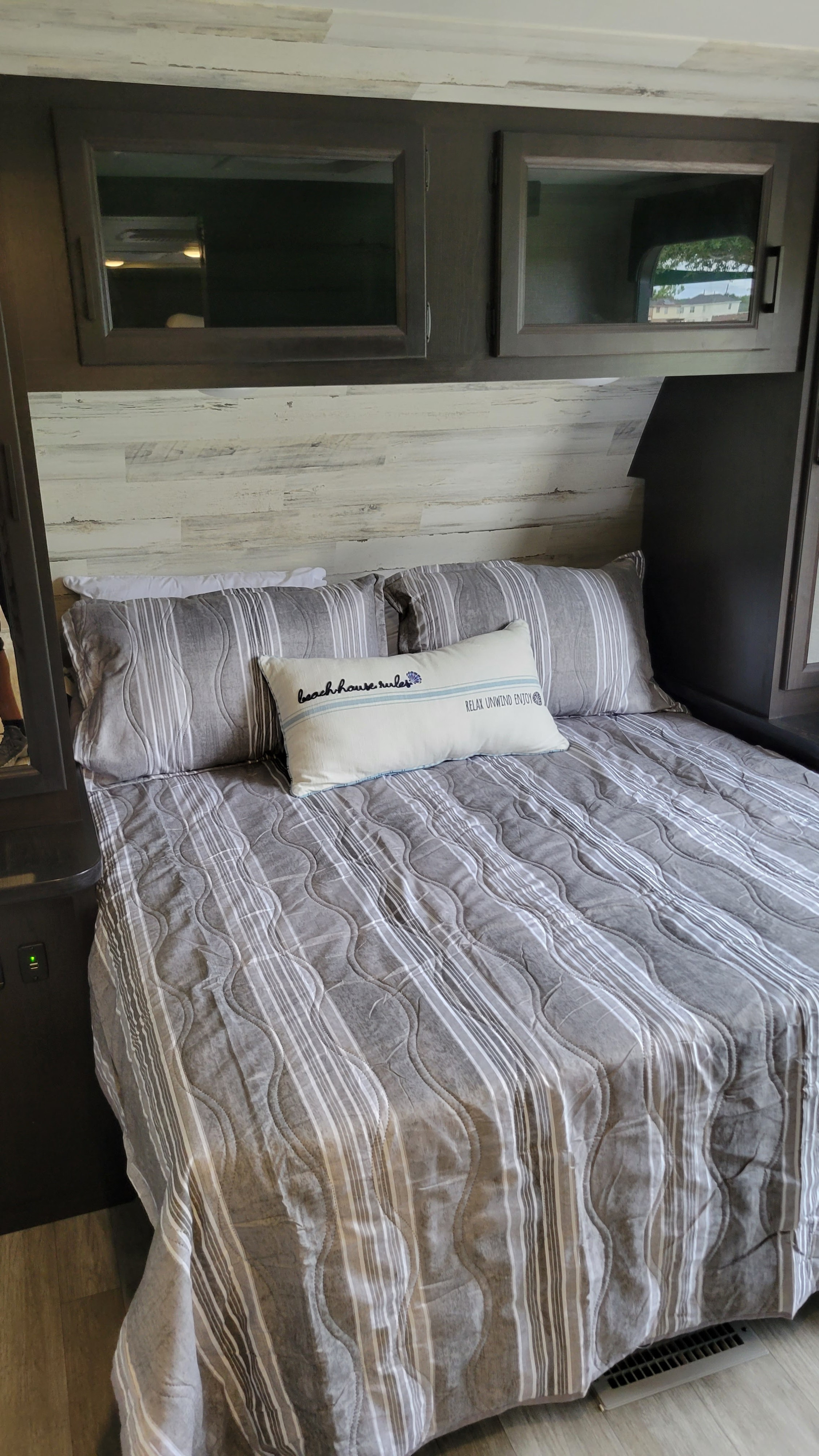 Cozy RV rental bedroom featuring striped bedding, a "beach house rules" pillow, and overhead storage cabinets.. Jayco Jay Feather 2022