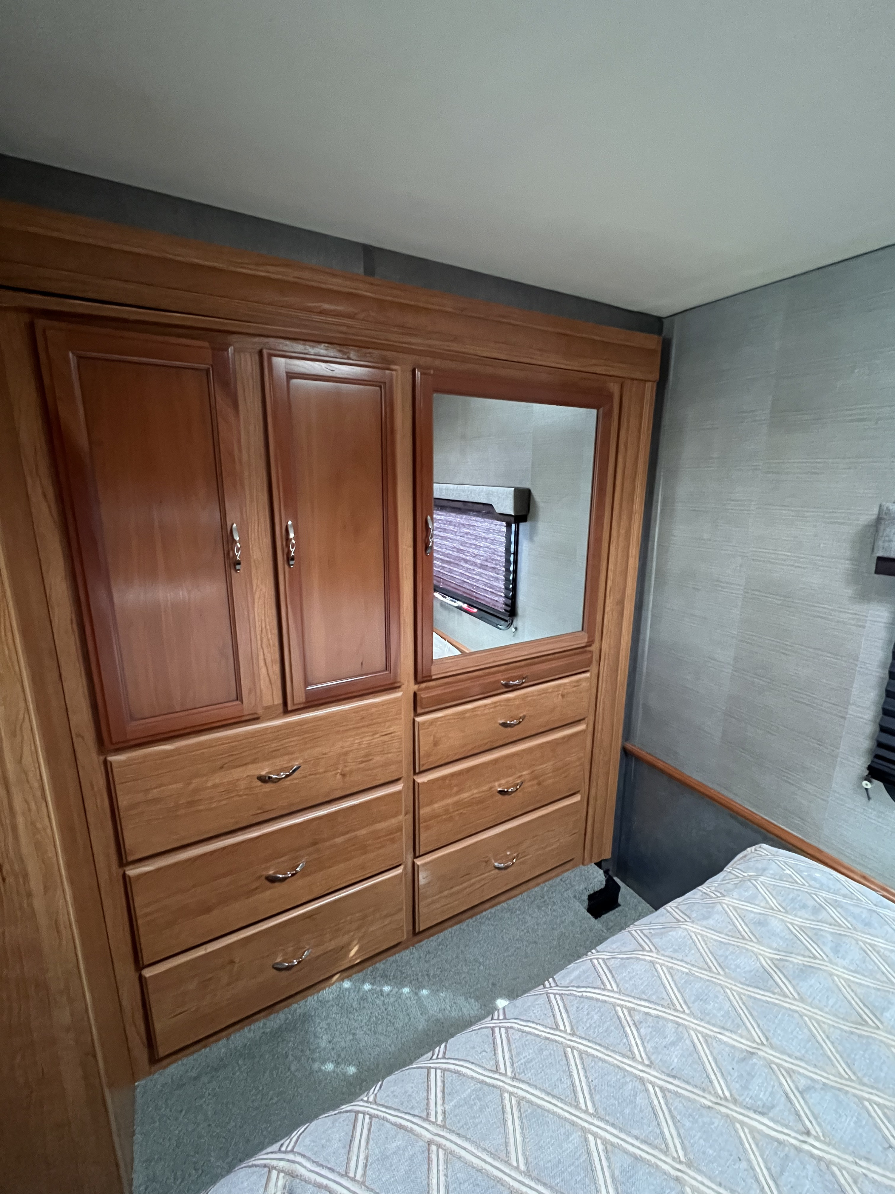 RV rental bedroom: Wooden wardrobe & dresser with mirror. Cozy bed with patterned bedding, on soft carpet.. Fleetwood Storm 2016
