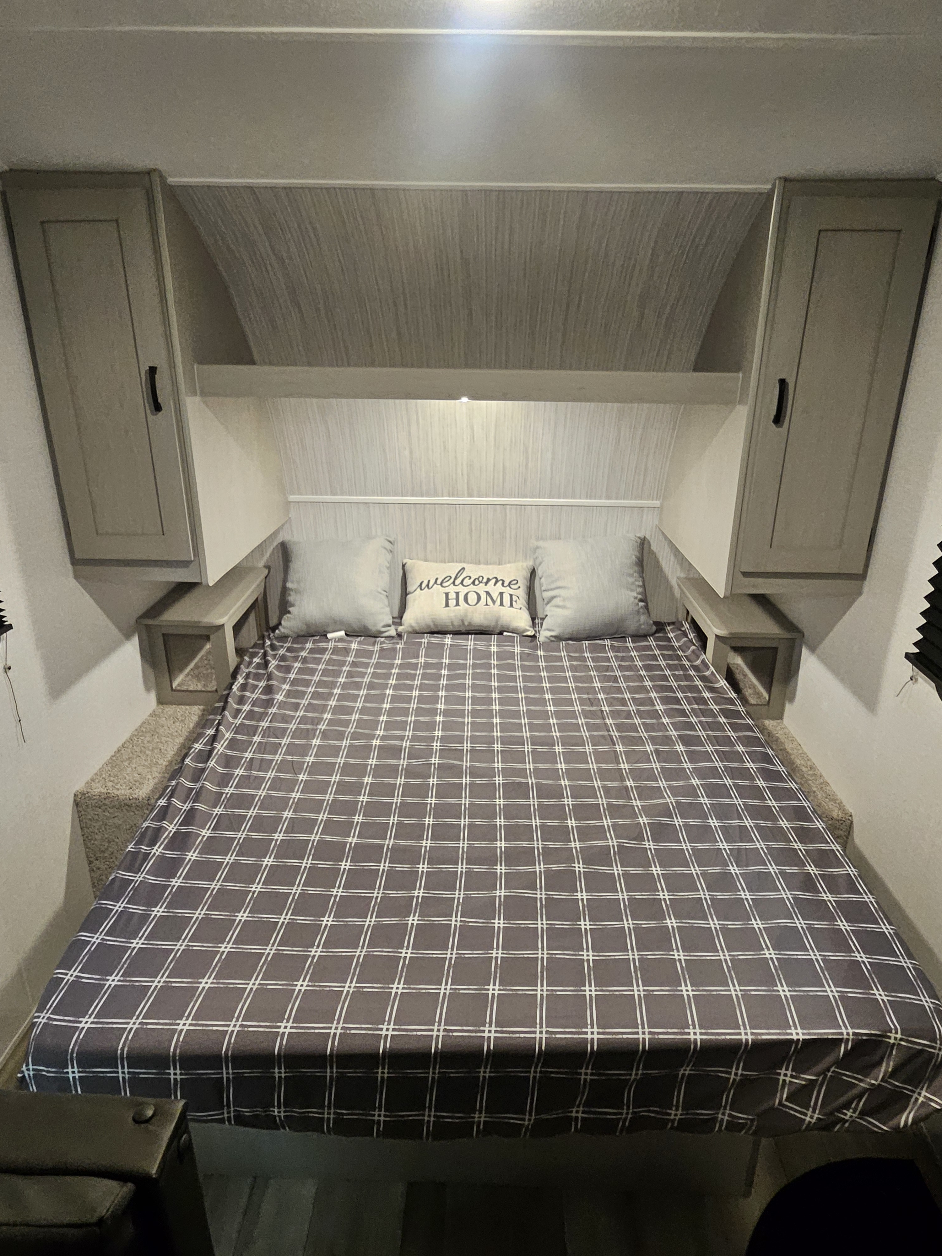 Cozy RV rental bedroom with plaid bedding, overhead cabinets, and a 'welcome HOME' pillow. Ideal for travel.. Forest River Clipper 17CFQ 2023