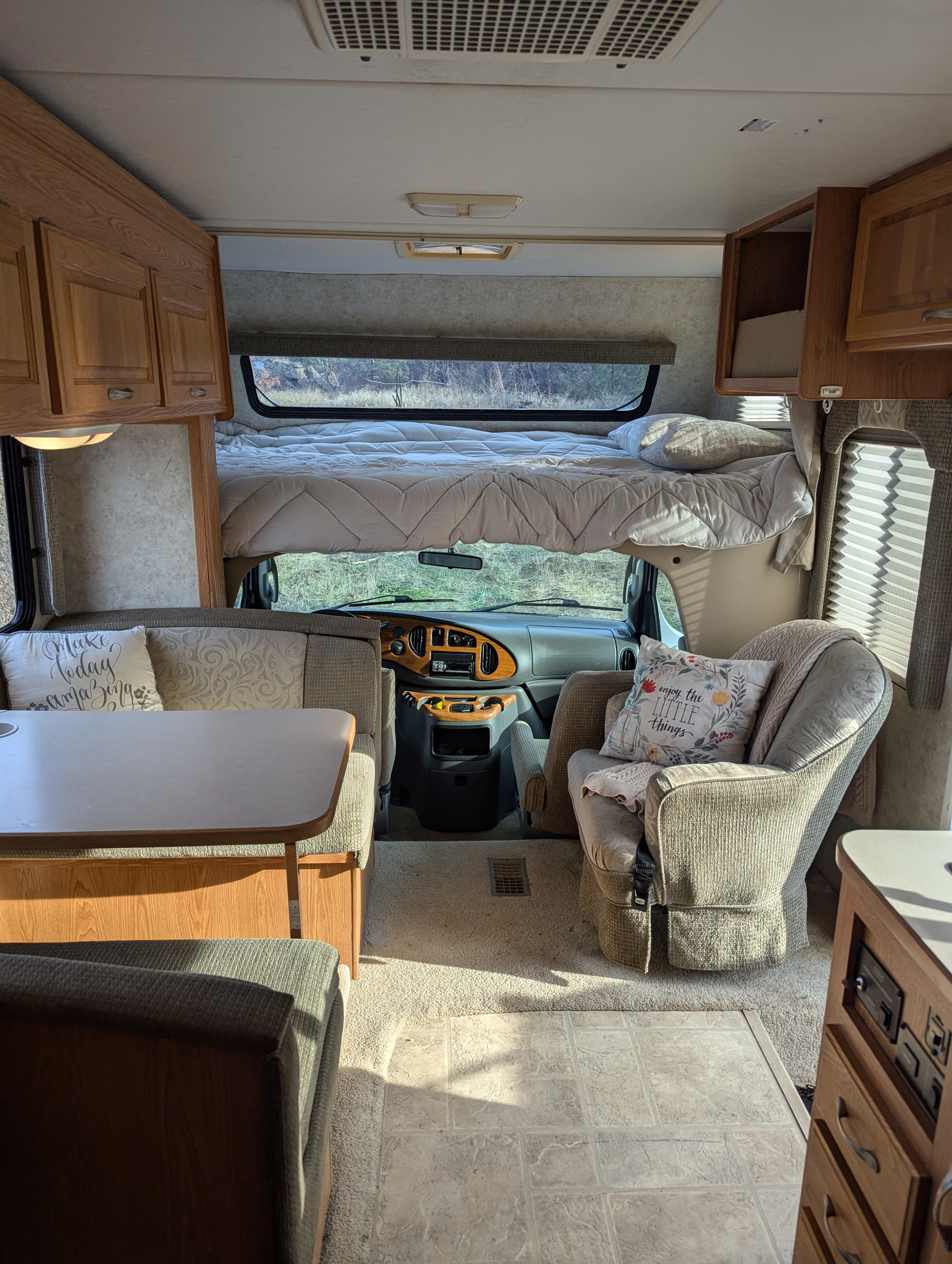 Spacious RV rental interior with a comfy bed above the cab, dinette area, and plush armchair.. Four Winds 5000 2005