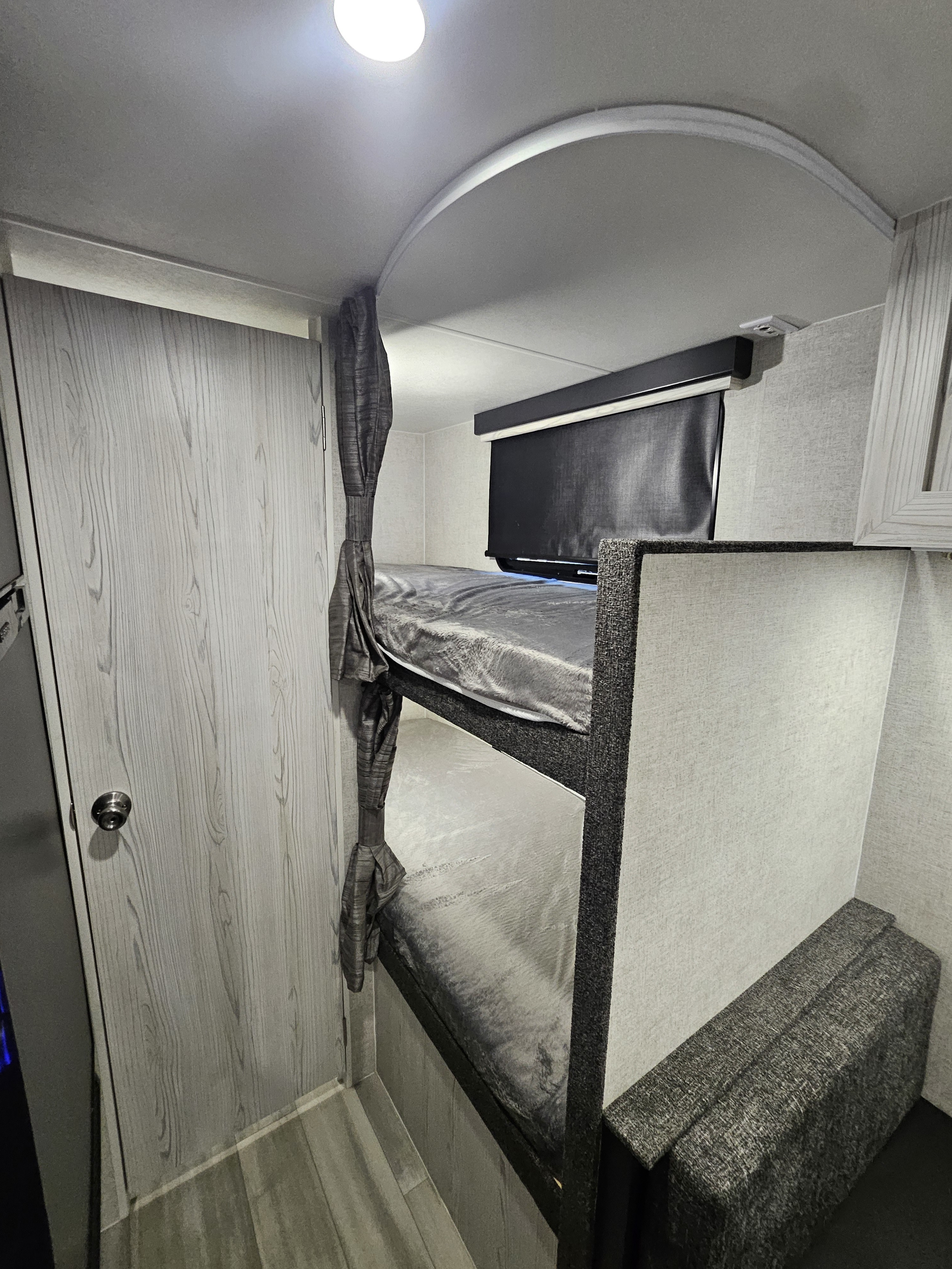 RV rental cabin: A bright bunk bed area with soft gray bedding, privacy curtains, a door, and textured walls.. Eclipse Milan 16MBH 2024
