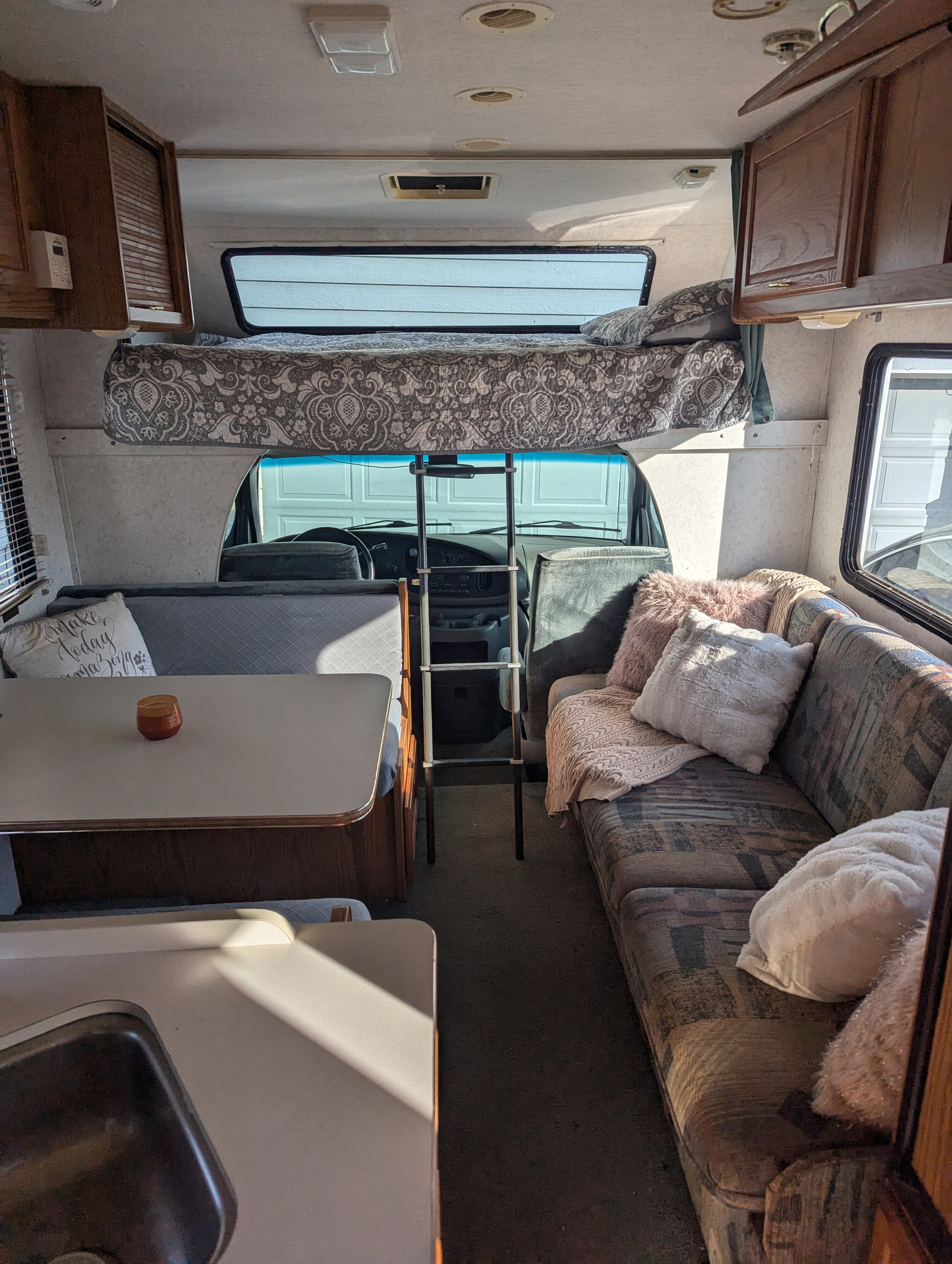 Cozy RV rental interior with a cab-over bed, dining area, lounge couch, and kitchen sink visible.. Itasca Spirit 2000