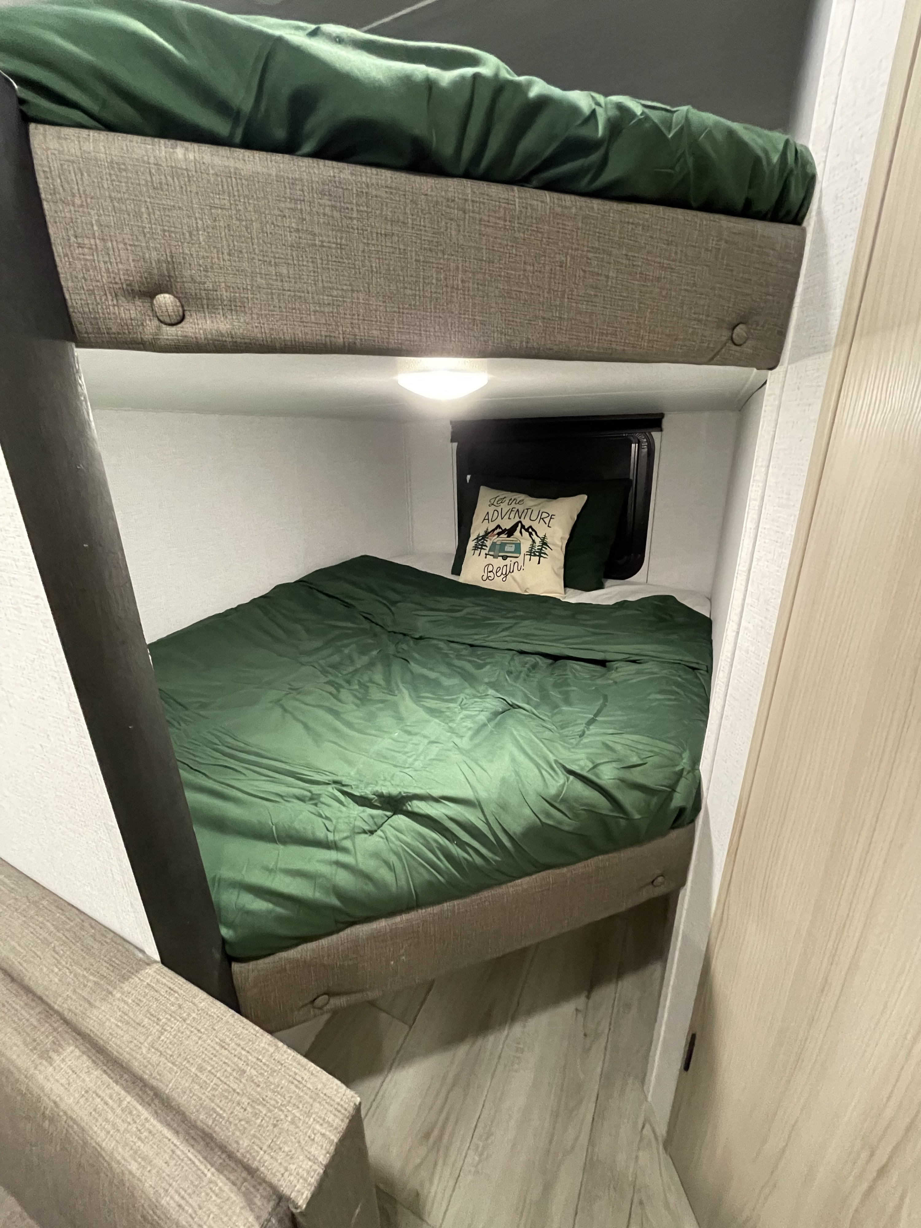 Cozy RV rental bunk beds with plush green bedding and an "Adventure Begin!" pillow. Ideal for travelers.. East to West Silver Lake 2025