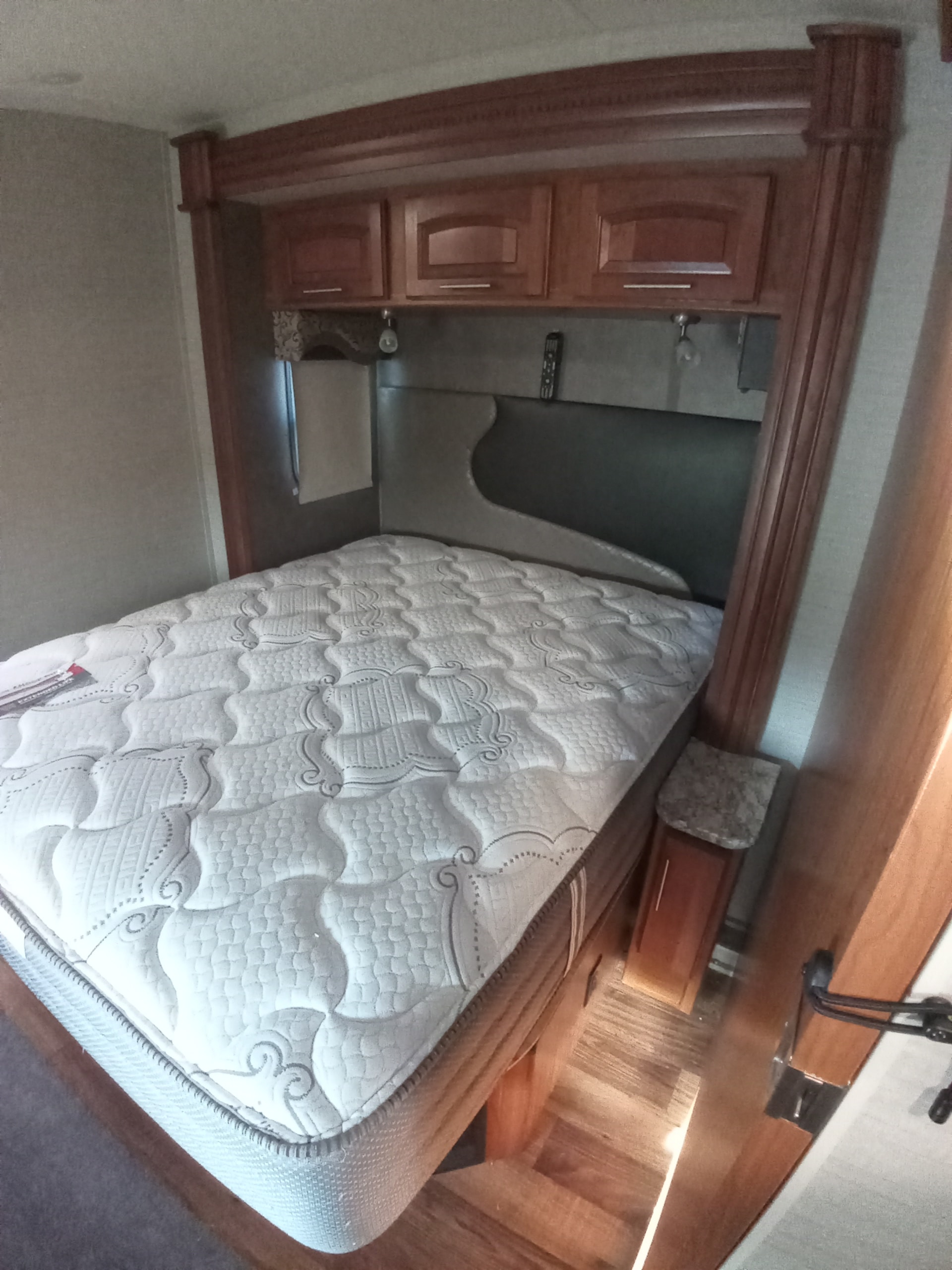 Inside an RV rental: a cozy bedroom with a quilted white mattress, sleek gray headboard, and warm wooden overhead cabinets.. Jayco Precept 2017