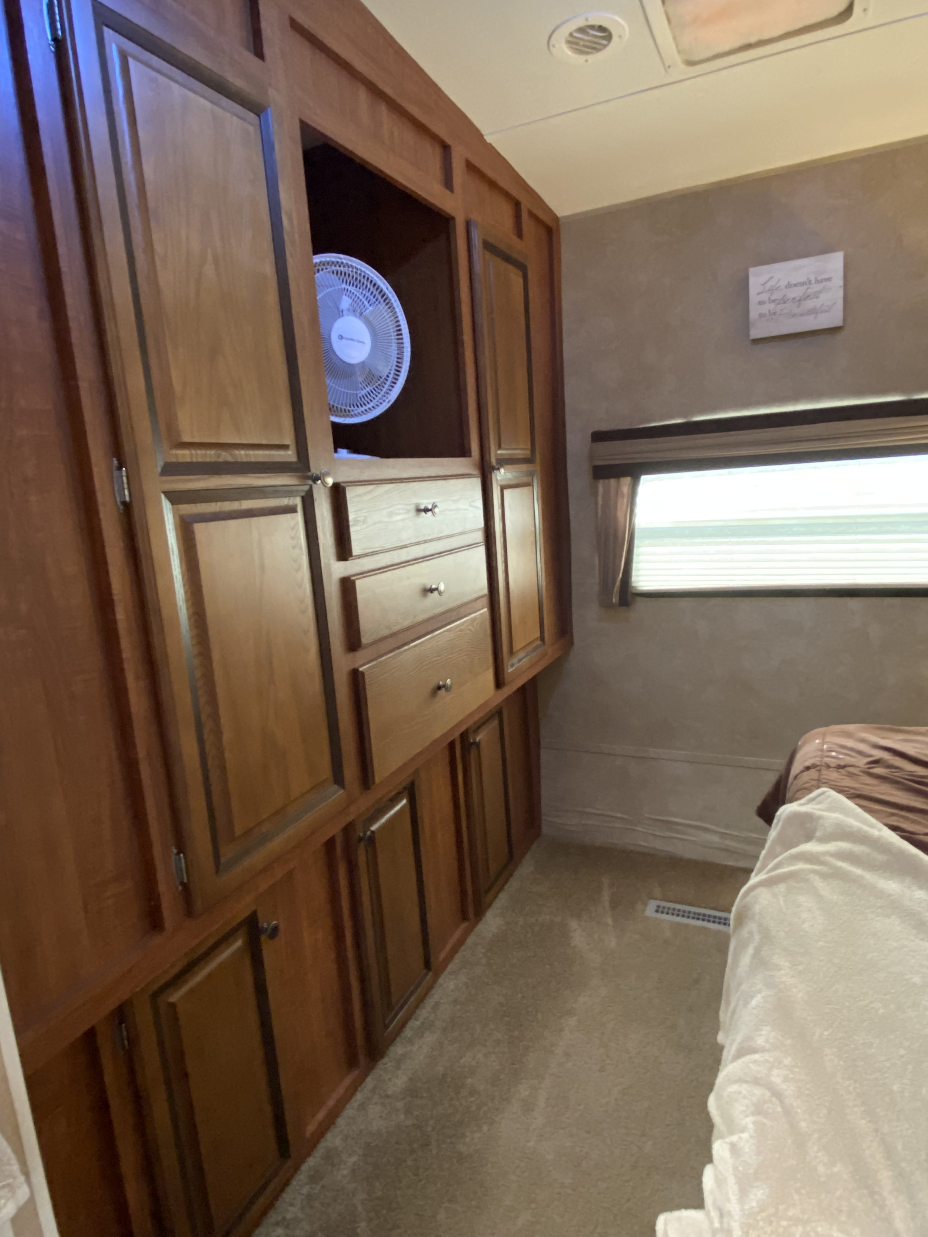 RV rental bedroom interior featuring extensive wooden storage cabinets, drawers, a fan, and window. Comfortable space.. Jayco Eagle Super Lite 2012