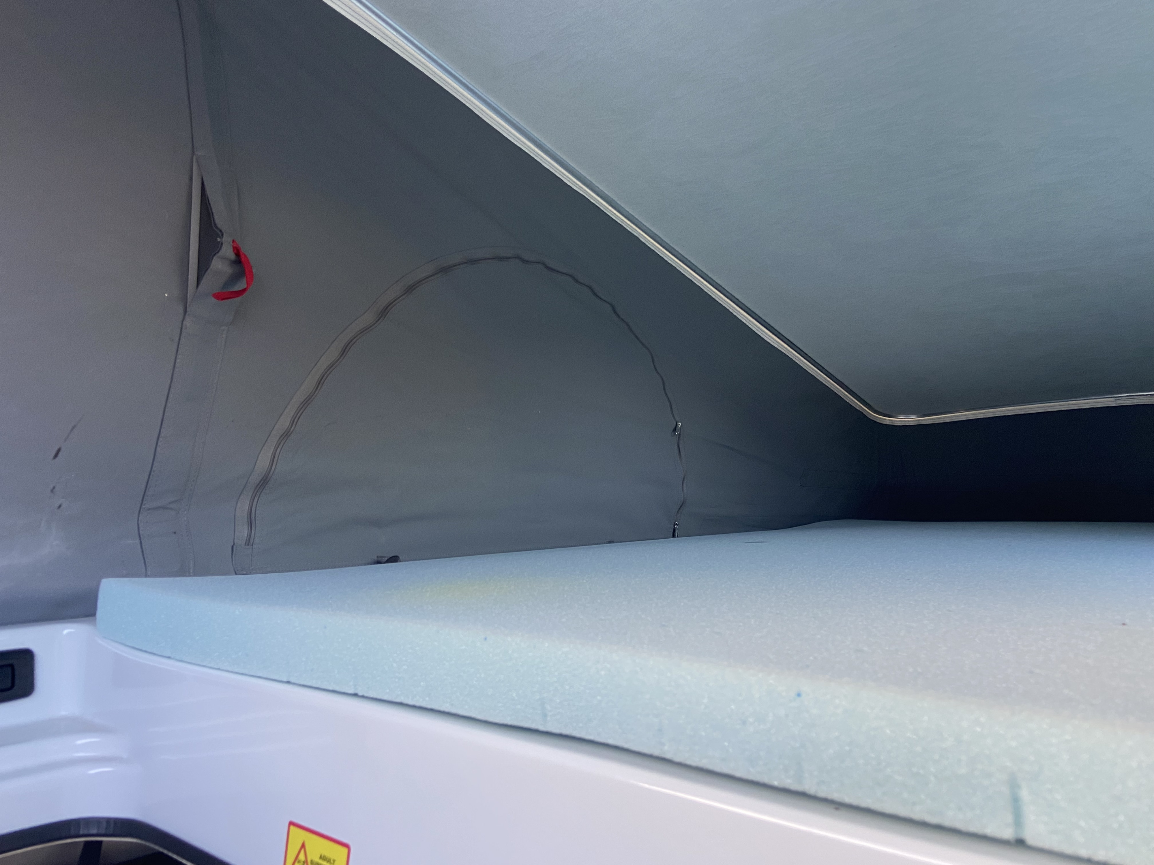 Interior view of a pop-top rv rental: comfy blue foam mattress in the sleeping area, surrounded by grey canvas.. Dodge Winnebago 2023