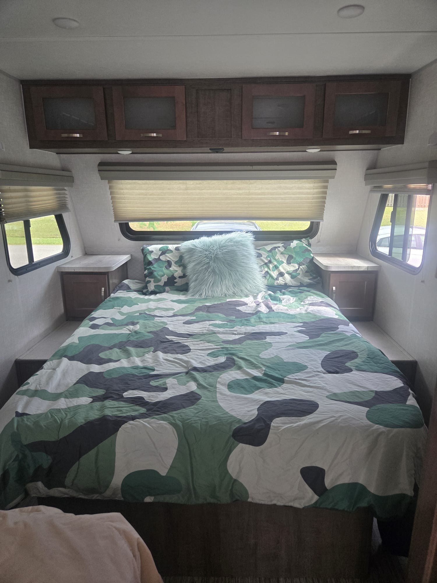 Inside an RV rental, this cozy bedroom features a bed with green camouflage bedding, side tables, and overhead cabinets. Ready for your trip!. No Boundaries 19.5 2020
