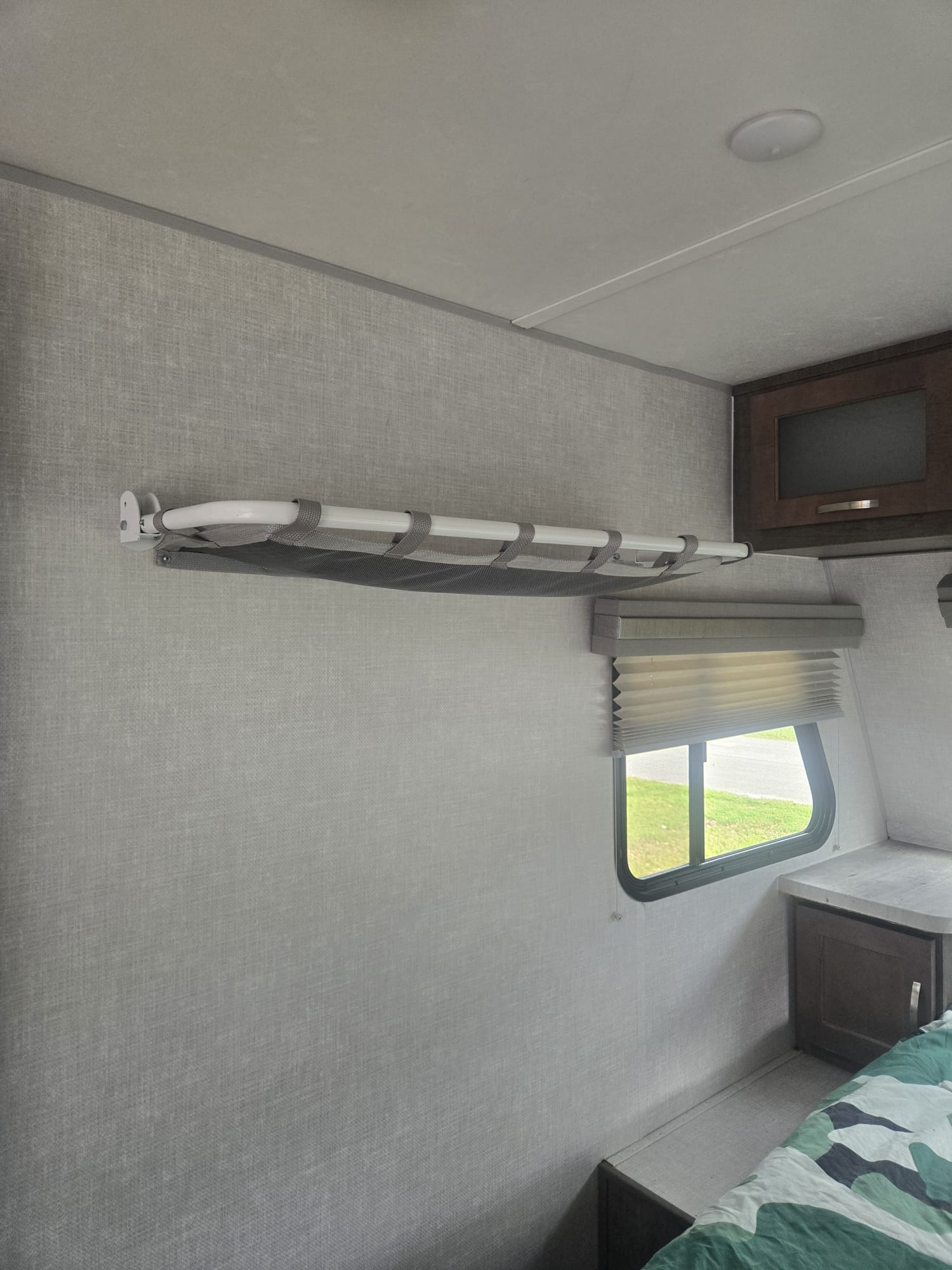 Compact living in an RV rental: a fold-down bunk/shelf on a textured wall, window with blinds, and bed with green camo bedding.. No Boundaries 19.5 2020