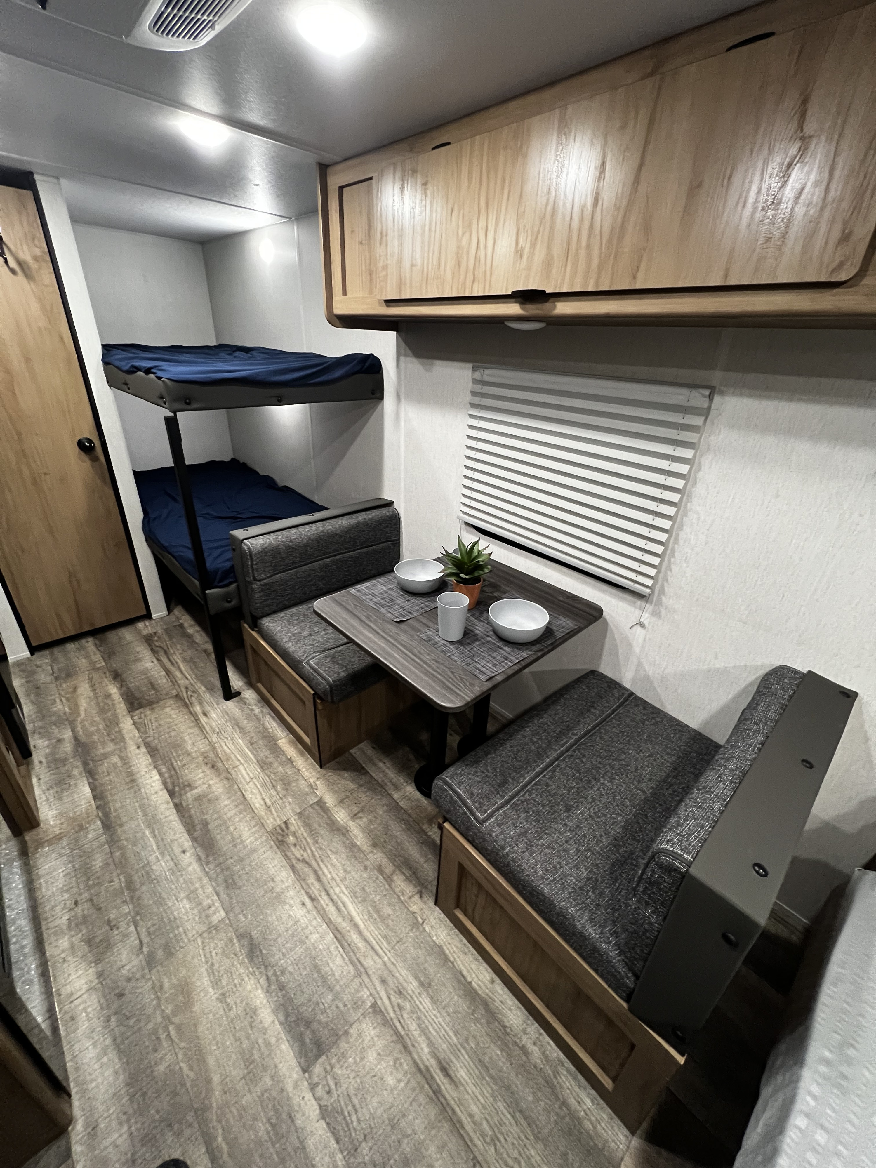 This RV rental interior features comfortable bunk beds, a cozy dinette with seating, overhead cabinets, and wood-look flooring.. Forest River Cherokee Wolf Den 16EV 2024