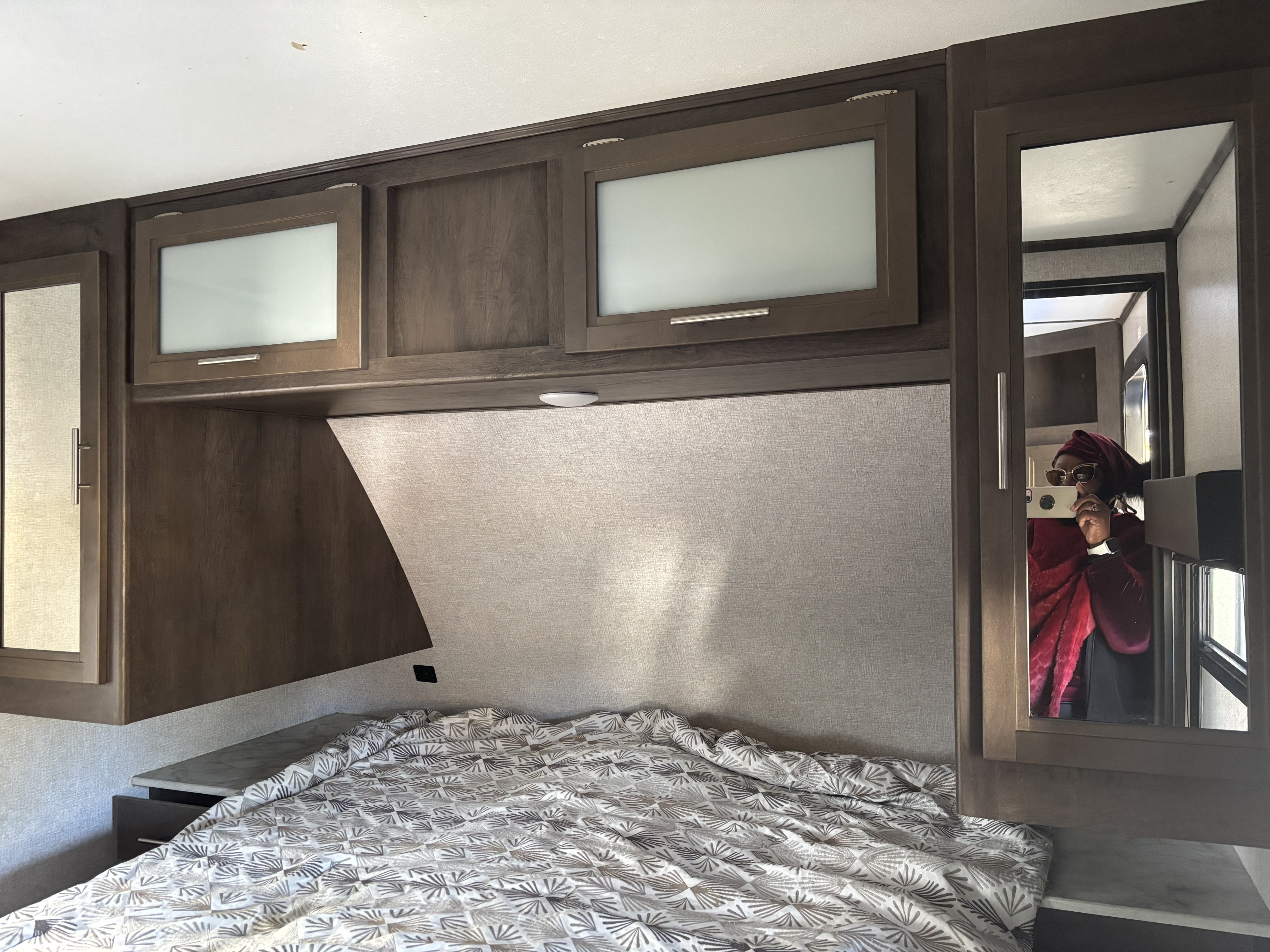 RV rental bedroom: a comfy bed with a patterned comforter, wood cabinets, & a mirror reflecting a person.. Other Other 2021