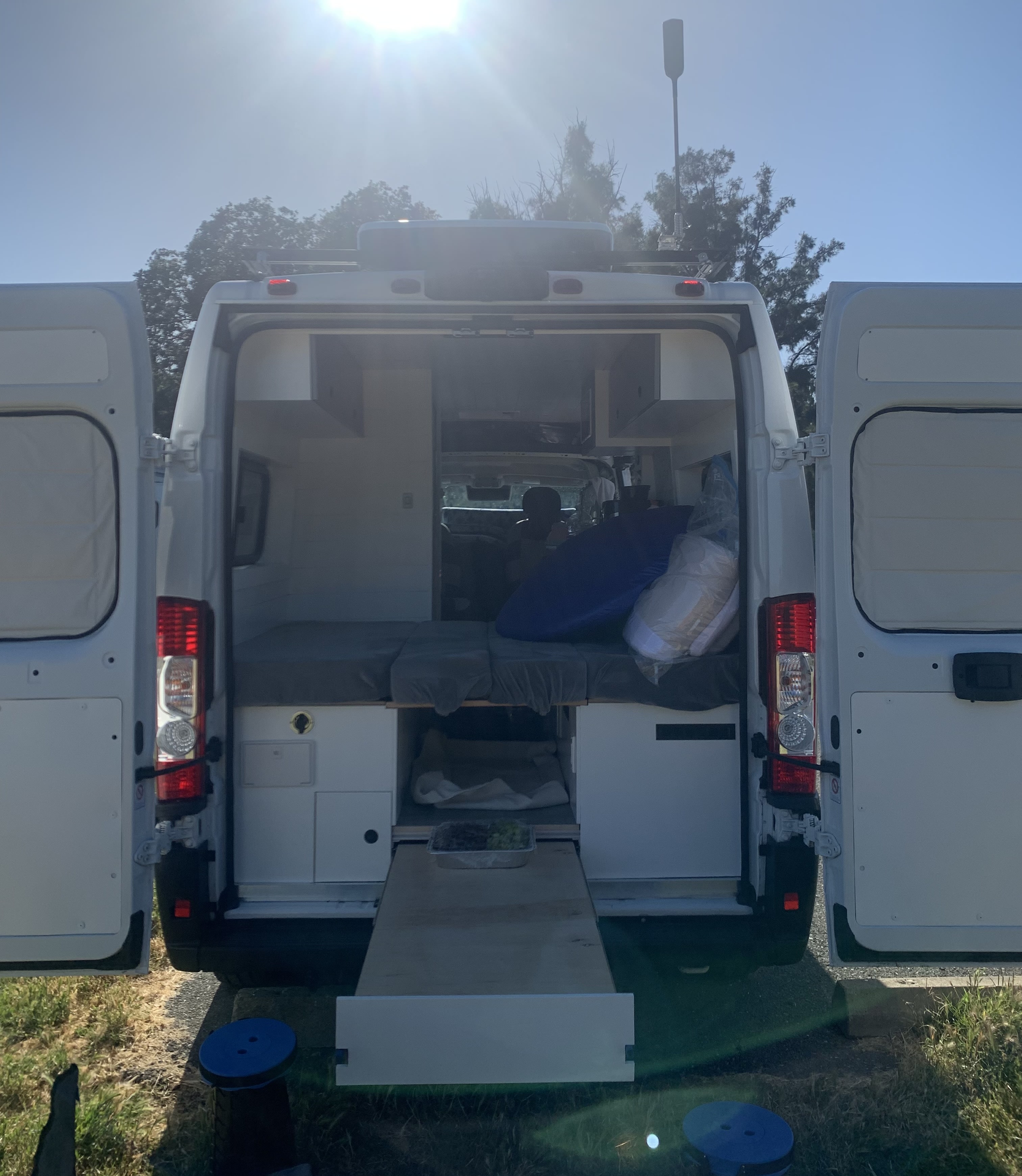 Open rear doors on this RV rental showcase a converted camper van interior: bed, storage, and pull-out tray. Ready for adventure!. Ram Promaster 2022
