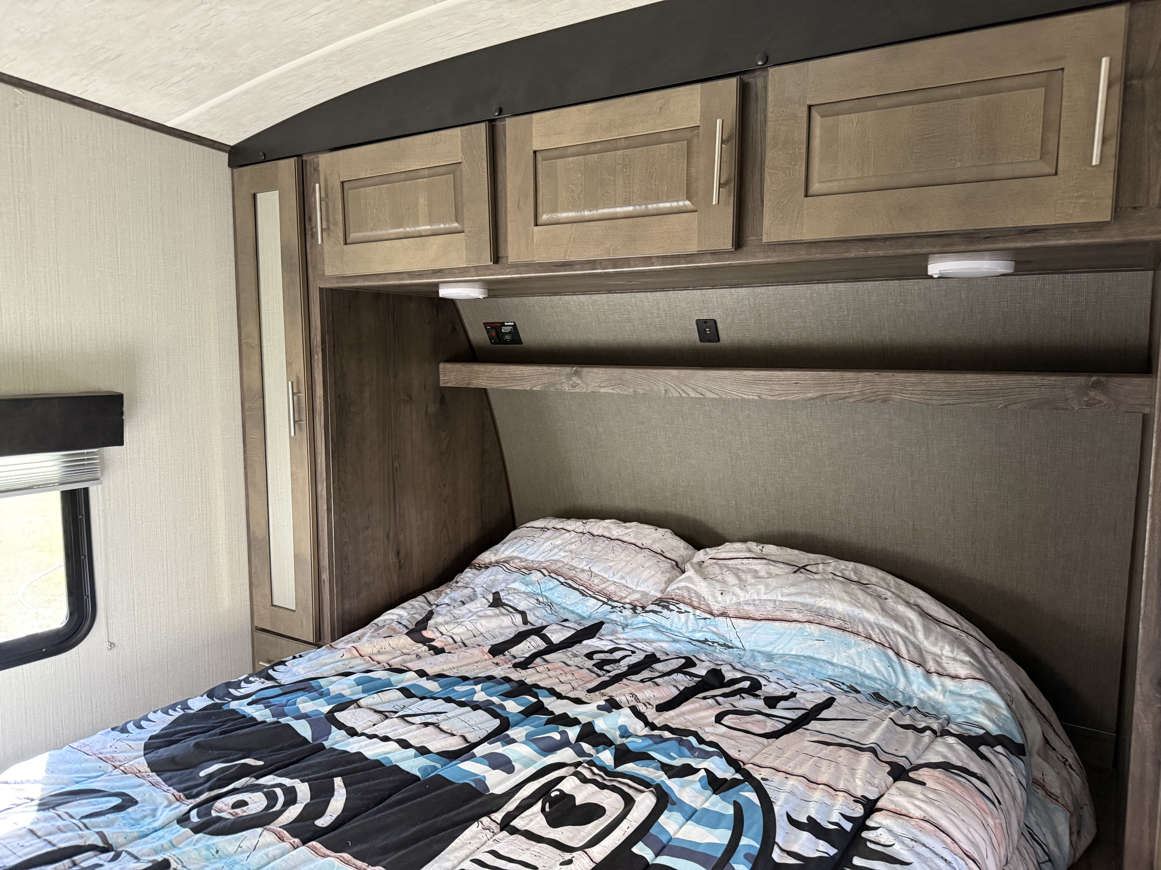 Cozy RV rental bedroom featuring overhead cabinets & comfy bed with built-in shelf. Ideal for travelers.. Heartland Torque 2019